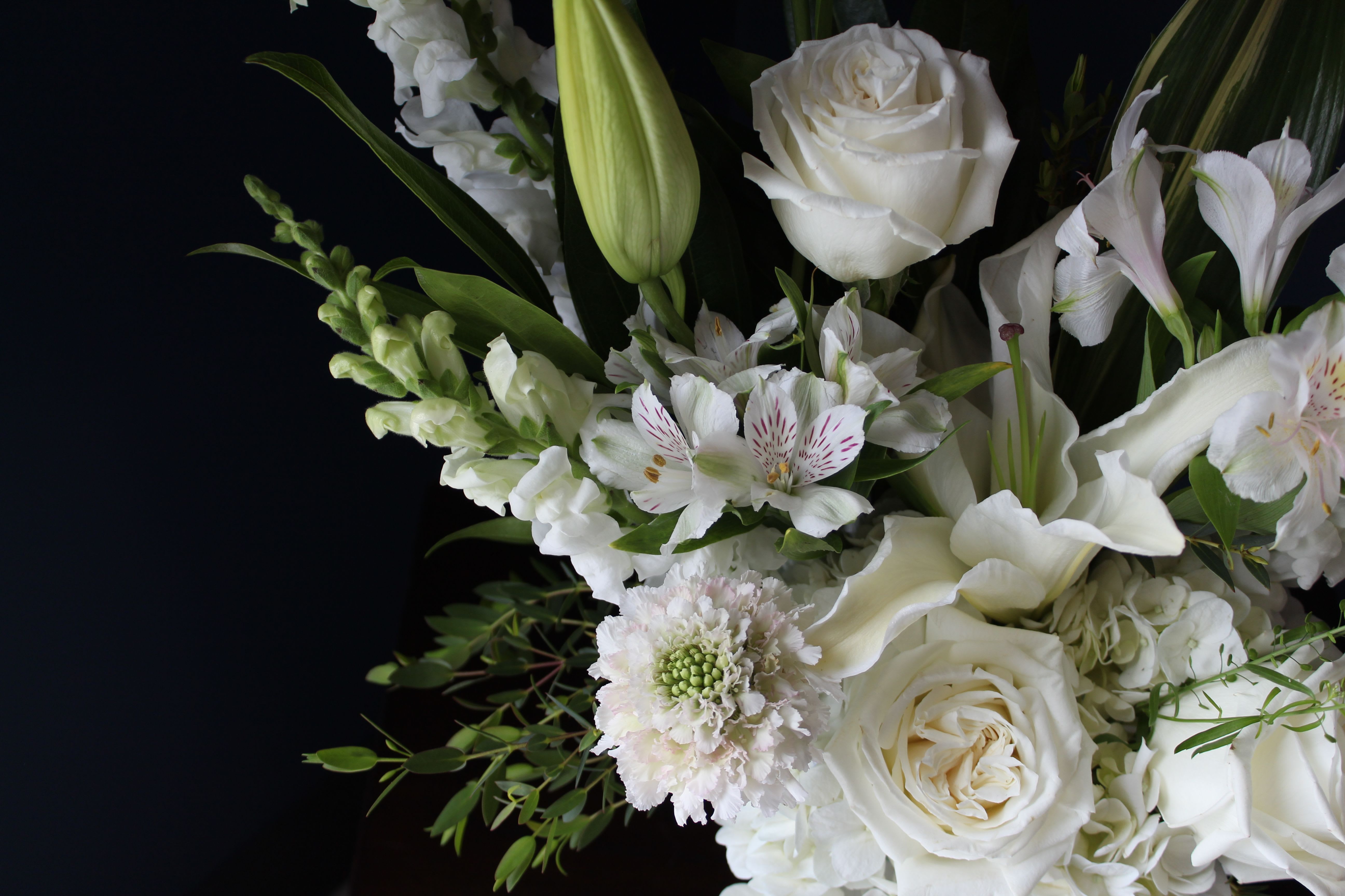 Elegance - An arrangement of white florals and greens in a clear vase. (Inquire about any color requests to enhance your gift)  For sympathy arrangements, we understand how important it is to create something truly meaningful. We would love for you to call us so we can discuss your needs and design a custom arrangement that best reflects your loved one’s life and spirit.
