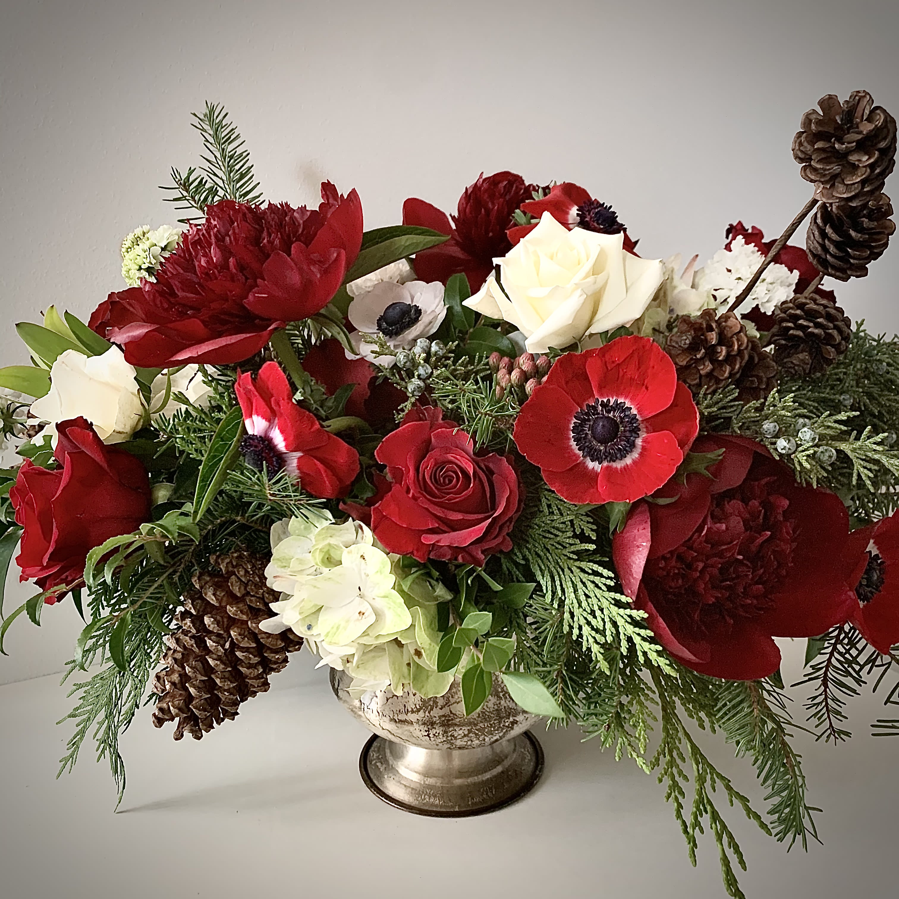 Good Tidings  - Spread joy this season with this display of anemones, roses, fresh evergreens and pine cones. 