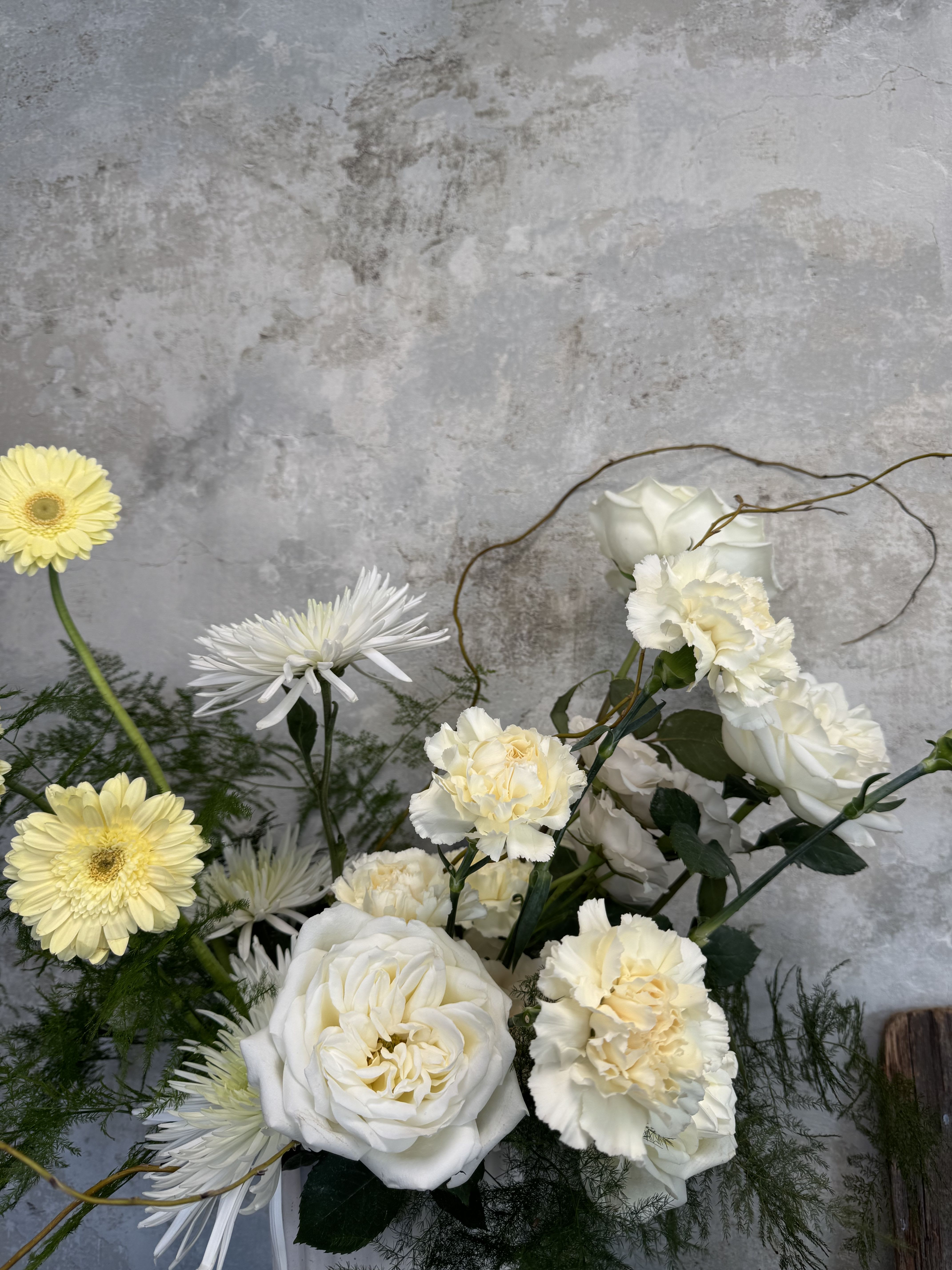 Quiet Muse Vase Arrangement - A gentle embrace in bloom: our Quiet Muse arrangement features lush whites, soft creams, and soothing greenery arranged in a white or clear vessel, designed to bring a sense of calm and thoughtful presence into a space. Overflowing with graceful stems that curve and drift freely, it reflects our signature organic style- whimsical, elegant, and soft.  This arrangement pairs creamy blooms with delicate textures and verdant foliage, creating an atmosphere of quiet reflection and stillness. Whether it’s delivered to a home, bedside, or as a meaningful gesture, Quiet Muse brings homage and hope in a gentle, understated way.