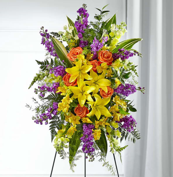 Celebration of Life - This bright and beautiful standing spray includes lilies, stock. roses and other complementary flowers. The photo pictured is a deluxe it will stand on a 60" easel. The standard will a less flowers,