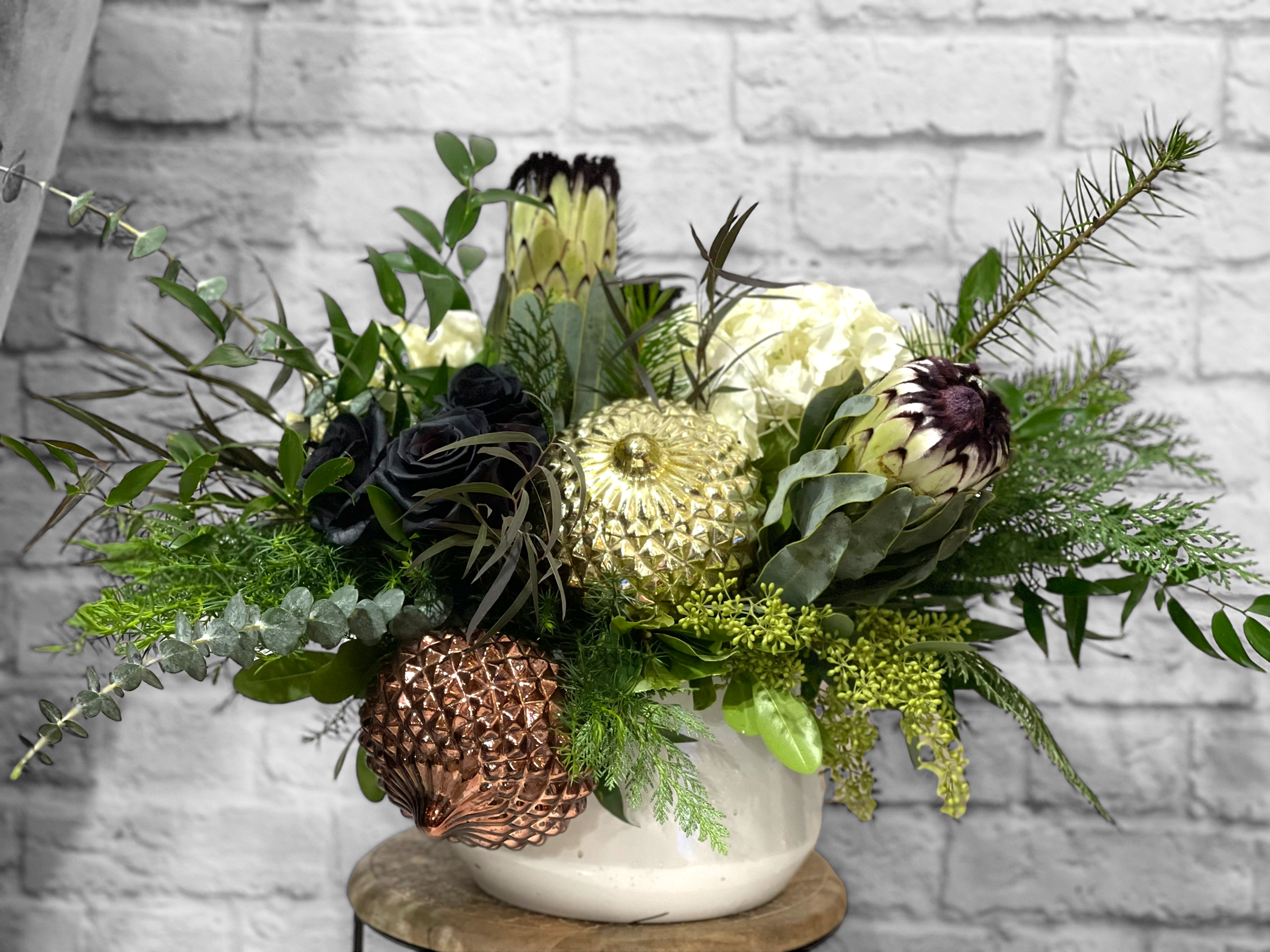 Christmas Creme - A stunning tone-on-tone floral arrangement with statement blooms and high quality glass ornaments. Includes rare white proteas, black roses, and white hydrangeas. 