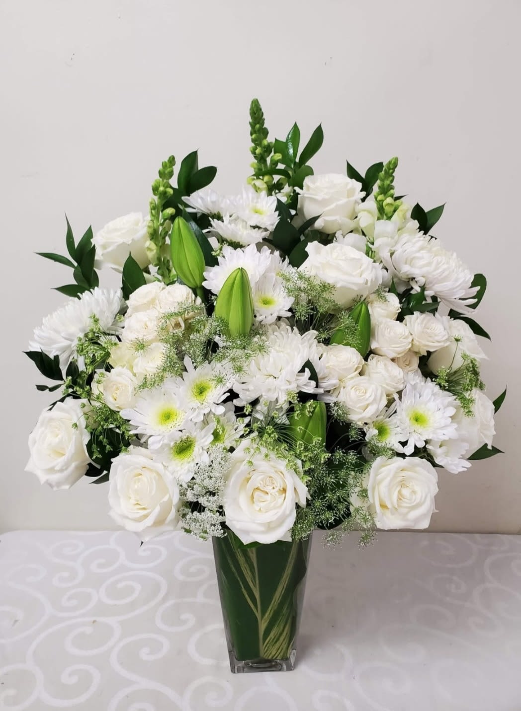 Thoughts of You - A serene arrangement of pristine white blooms nestled in a glass lined with ti leaves, is designed to convey compassion during difficult times. This thoughtful composition offers quiet comfort and grace, allowing your heartfelt sympathy to speak volumes. Perfect for honoring a cherished memory with understated beauty and dignity.  AS PICTURED: PREMIUM 16&quot;W by 20&quot;H