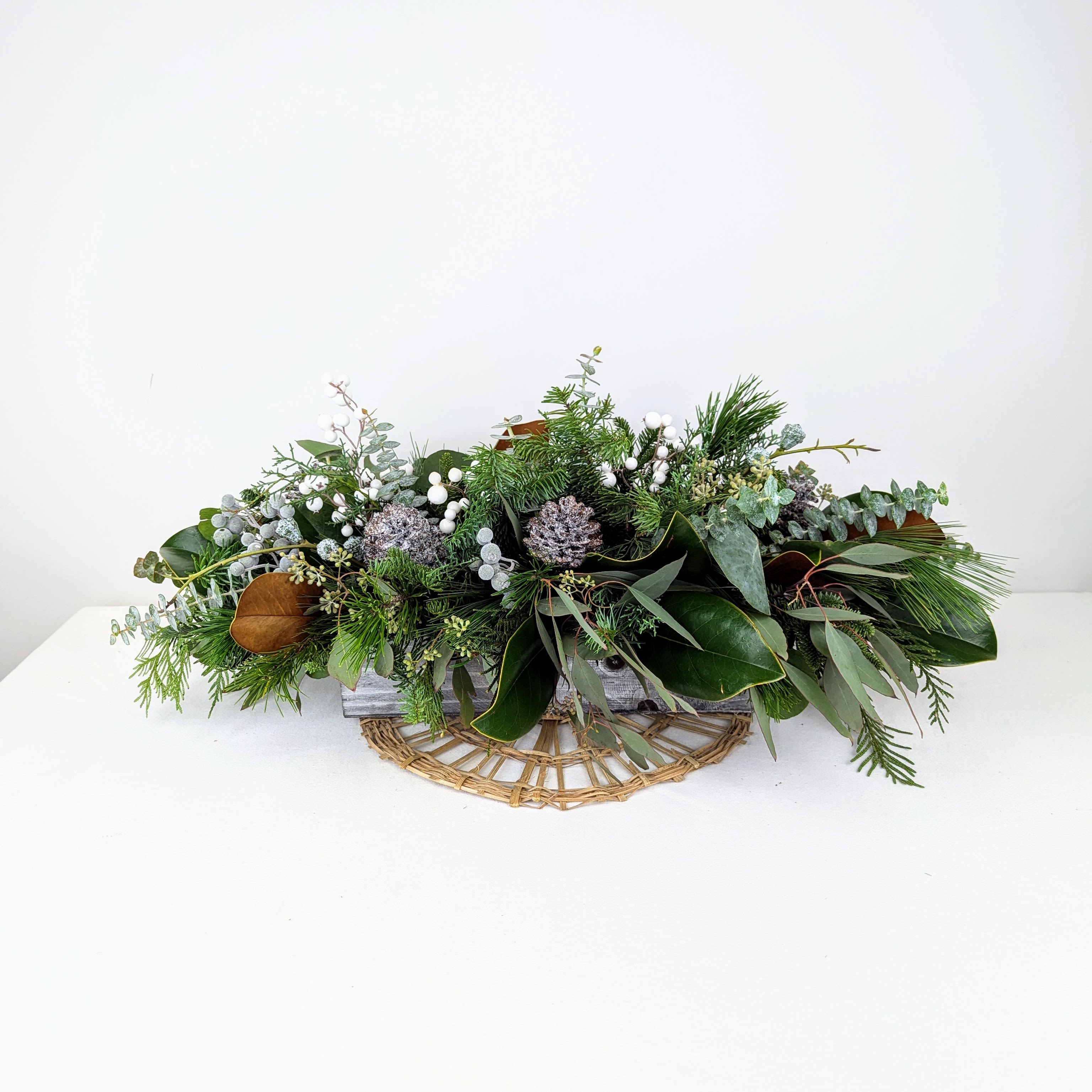 Woodsy Retreat - A simple, natural and elegant holiday centerpiece that brings the outdoors, in! A fragrant mix of evergreens, eucalyptus, pinecones, berries and magnolia leaves nestled in a rectangular wooden box.  Upgrade to the deluxe to add some candlelight to your dinner table.