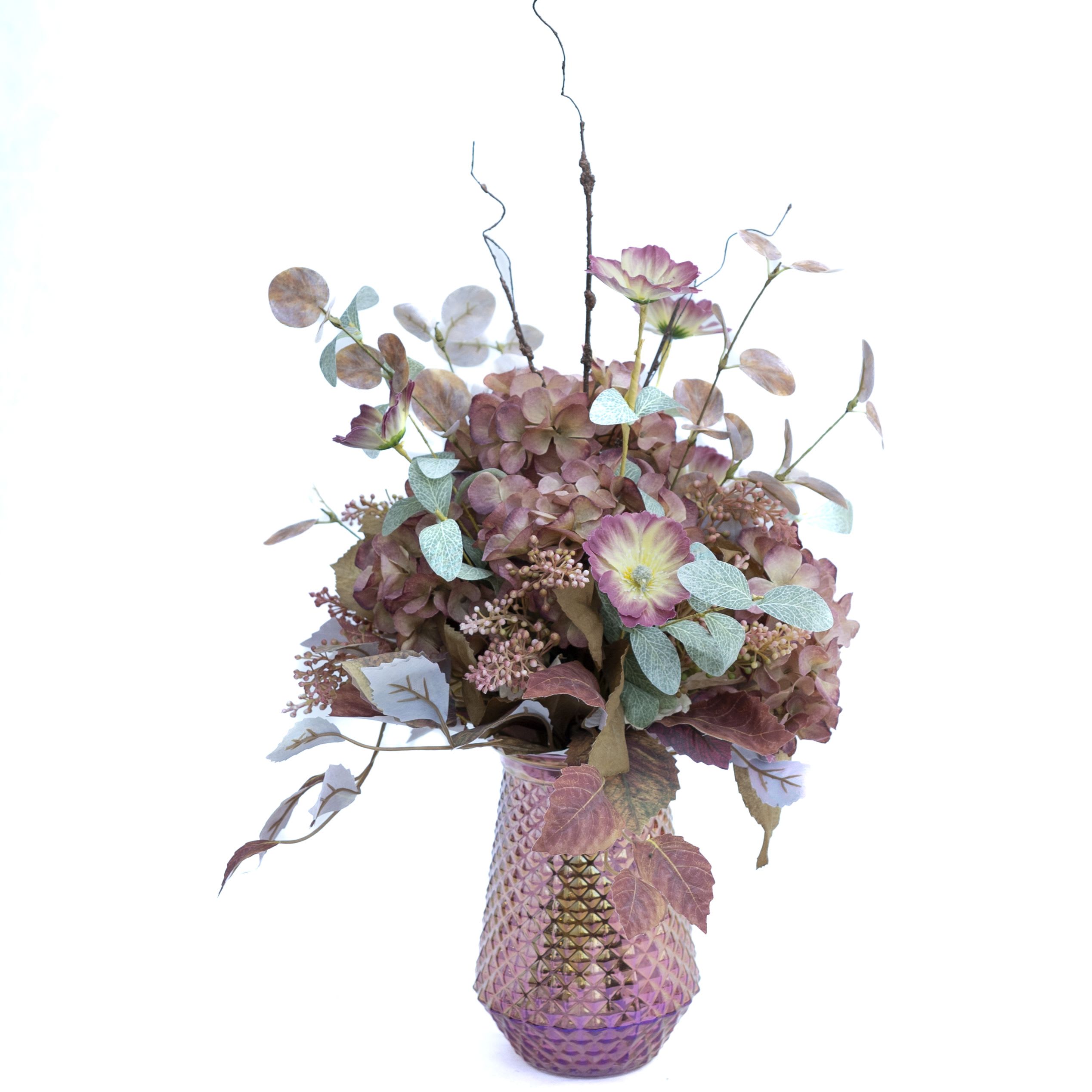 Blush Garden Luxury Arrangement - Add a touch of refined elegance to your space with the Blush Garden Luxury Arrangement. This exquisite floral display showcases soft, muted pink hydrangeas, delicate primroses, and frosted eucalyptus branches, creating a sophisticated blend of textures and colors. The arrangement is beautifully presented in a stunning iridescent, diamond-patterned vase, which enhances the romantic, vintage-inspired feel of the piece. Perfect for enhancing a living room, bedroom, or special event space, this arrangement offers timeless beauty with no maintenance required.  Height: Approximately 24 inches Unique iridescent vase included Elegant design suitable for all decor styles Perfect for gifting or enhancing home décor This luxurious display is ideal for those looking to bring a soft, romantic ambiance to any setting.