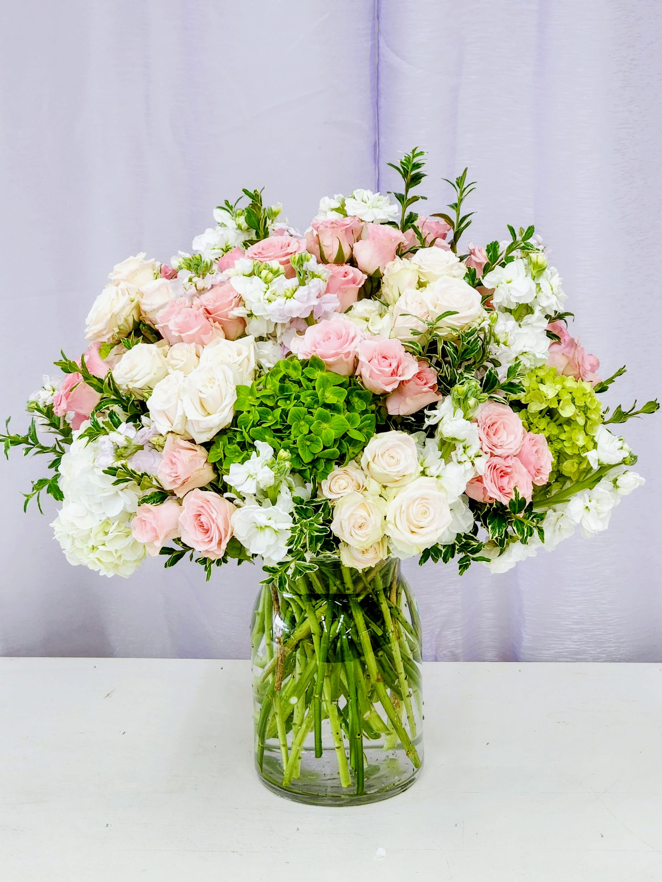 Soothing - Bring calm and charm to any space with our Soothing arrangement—a delightful mix of green and white hydrangeas paired with soft pink and white blooms, all nestled in a crystal-clear vase. This cheerful composition strikes the perfect balance between serene and spirited, making it ideal for brightening someone's day or adding a gentle pop of color to your home. Fresh, elegant, and oh-so-easy on the eyes. AS PICTURED: PREMIUM 15&quot; WIBE BY 18&quot; TALL