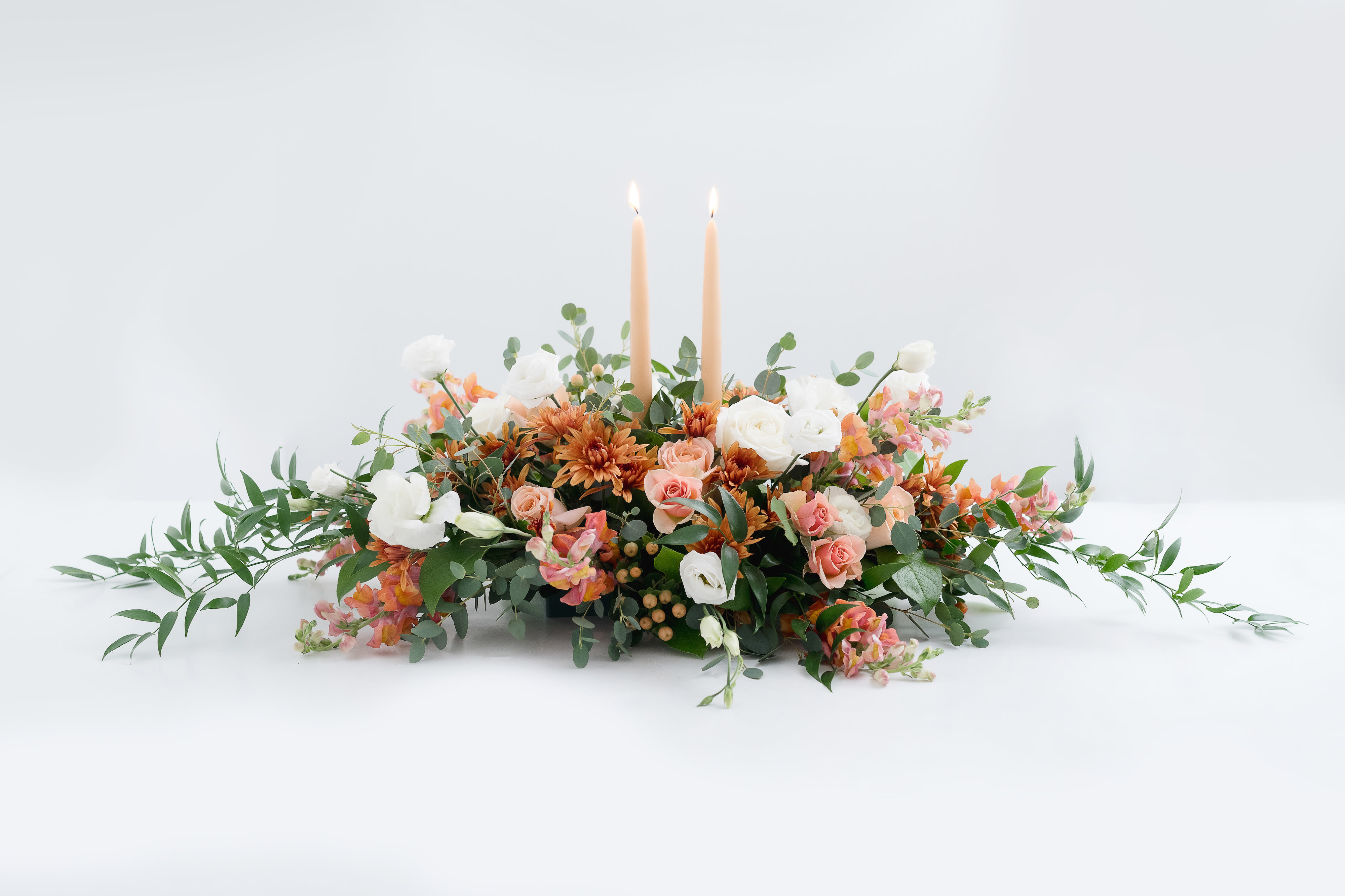 White Pumpkin  - An elegant and soft take on Fall colors for the sophisticated table. Roses, mums, Snapdragons and berries with Eucalyptus make up this centerpiece with Gold Spice taper candles. GORGEOUS! The perfect gift to send or to adorn your Thanksgiving table.   This arrangements is approximately 20&quot; long and 10&quot; wide. 