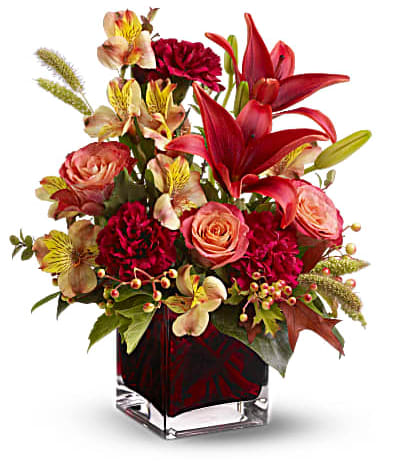 Teleflora's Indian Summer - As bright and intense as a hot Indian summer afternoon, this deep red, orange and burgundy bouquet - complemented by autumn-hued oak leaves and feathery millet - is arranged in a modern glass cube vase that's a luscious shade of plum. Who wouldn't love to receive such a gift? Orange roses and alstroemeria, red Asiatic lilies, burgundy carnations, huckleberry and berries - accented with artificial oak leaves and millet - are arranged in a plum glass Teleflora cube vase. Orientation: All-Around