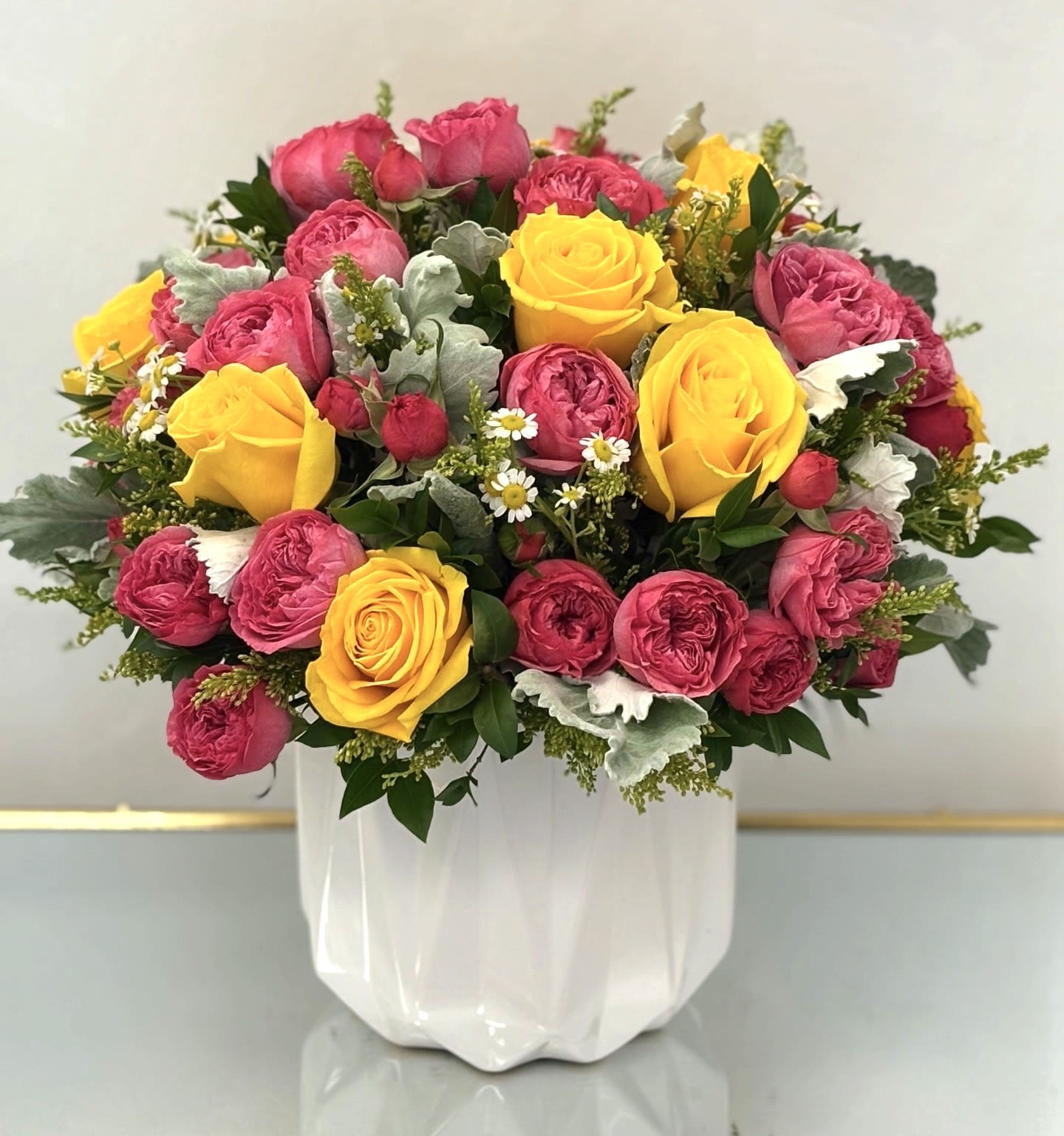 Raspberry Sunshine By VLM Flowers - Raspberry Sunshine is a bright and joyful bouquet bursting with personality. Bold yellow roses and rich raspberry garden roses are playfully accented with chamomile, dusty miller, and soft greens, all beautifully arranged in a crisp white ceramic vase. A perfect way to share warmth, cheer, and positive energy for any celebration or thoughtful surprise.