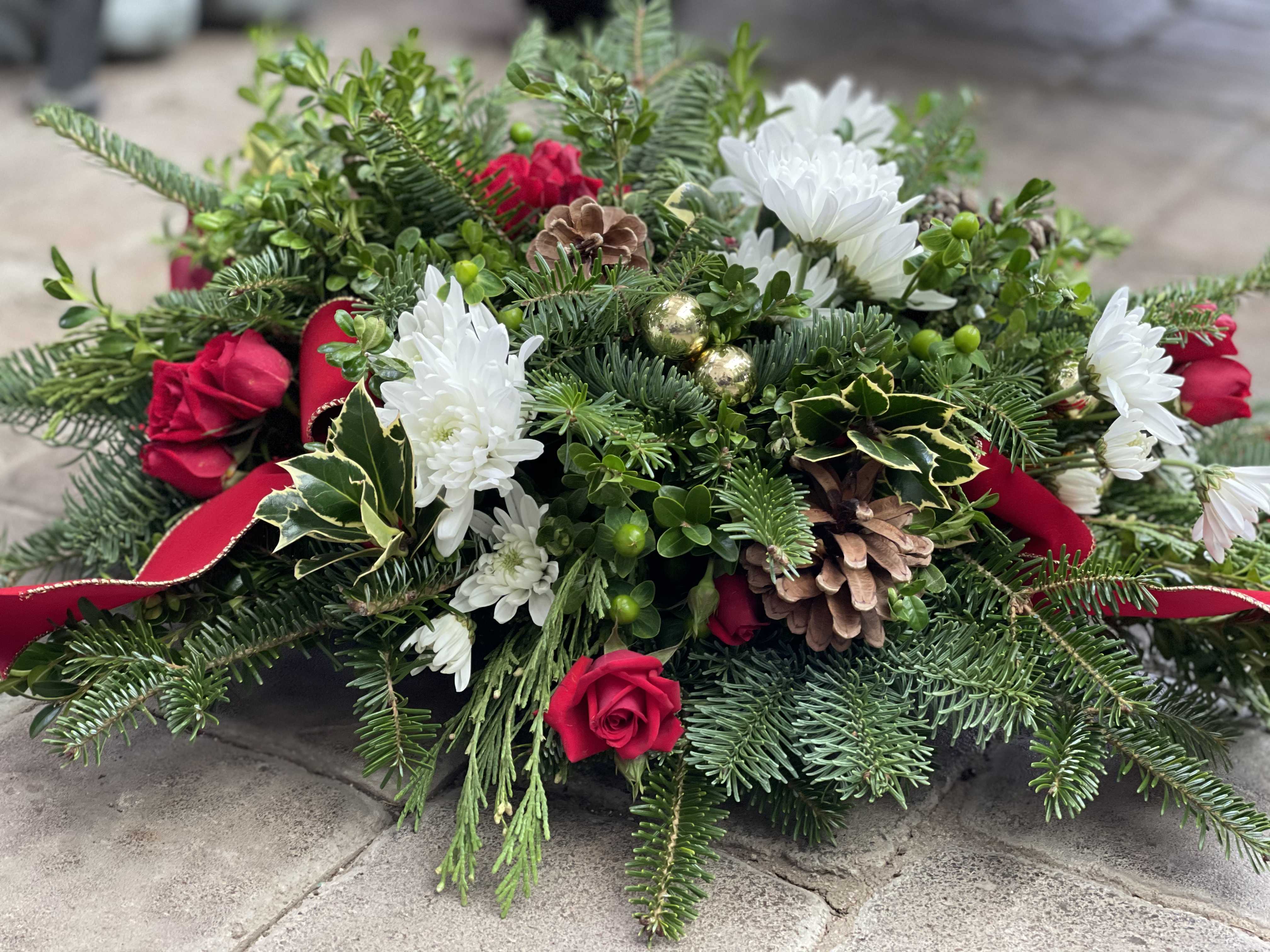 Yuletide Centerpiece (without candles) - Simplistic Elegance. This oblong, evergreen centerpiece is a perfect hostess gift.  The evergreen base will last for weeks and the holiday accents can be easily removed.  Enjoy this beautiful centerpiece for the whole season.  No candles are included in this design.   This arrangement is created in a design tray so you will not see a container and the arrangement will appear to be sitting directly on your table.  To keep your blooms lasting longer, add water to the design tray every few days.