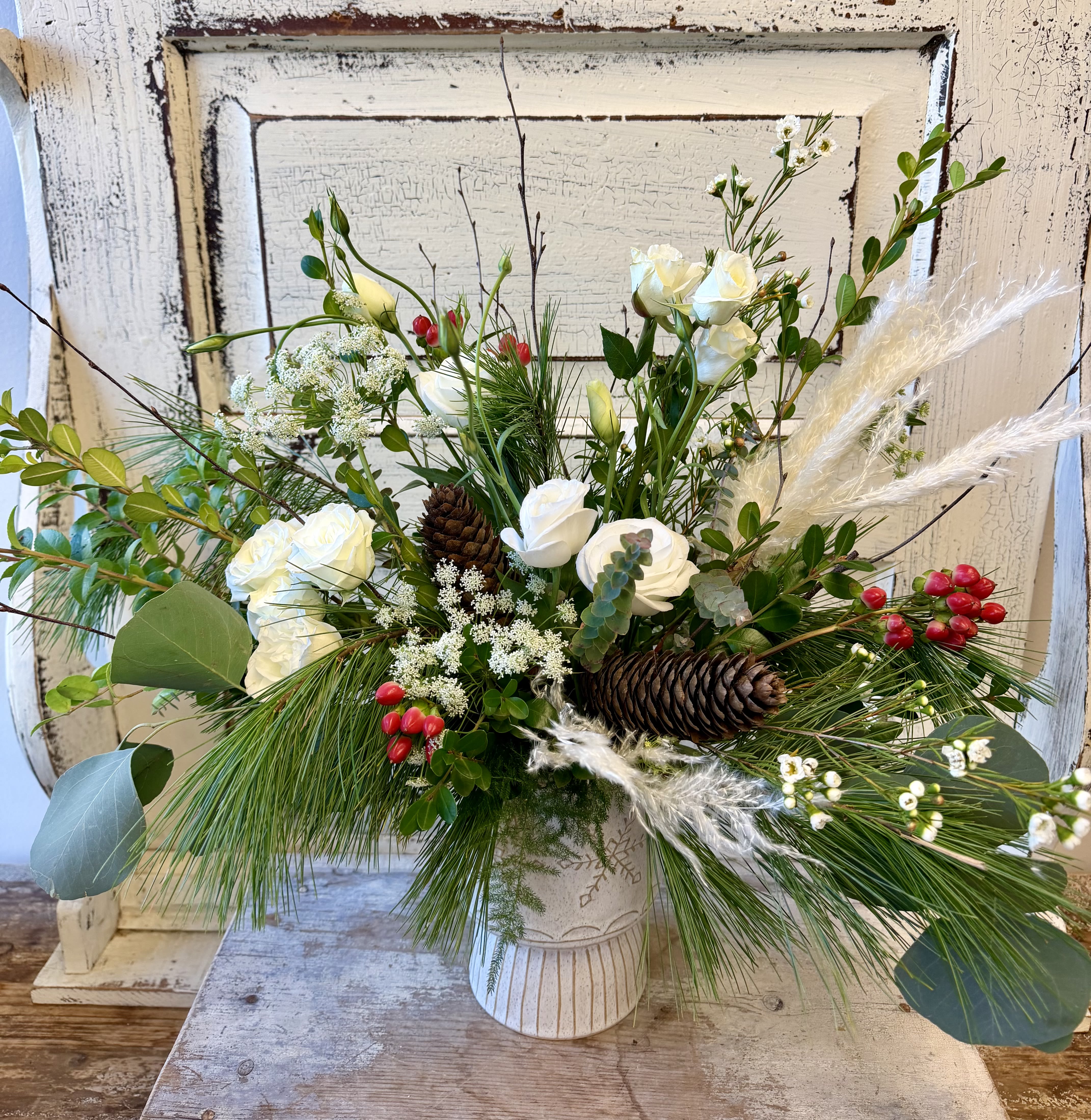 White Christmas - A beautiful design for the holiday season, this ceramic pedestal dish is carved with snowflakes and can double as a candle holder when inverted. The container is filled with evergreens, mostly white flowers and an accent of red berries and pine cones. Flower options will vary based on inventory.