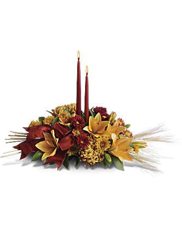 Graceful Glow Centerpiece  - Add a graceful glow to your Thanksgiving dinner table or fall-decorated foyer with this warm, seasonal arrangement. Lilies, mums and asters are accented with sprays of wheat below glowing taper candles. This classic Thanksgiving centerpiece features orange asiatic lilies, red matsumoto asters, bronze disbud mums, bronze daisies and bronze cushion mums. Burgundy satin ribbon, stems of wheat, and two taper candles add seasonal sophistication.