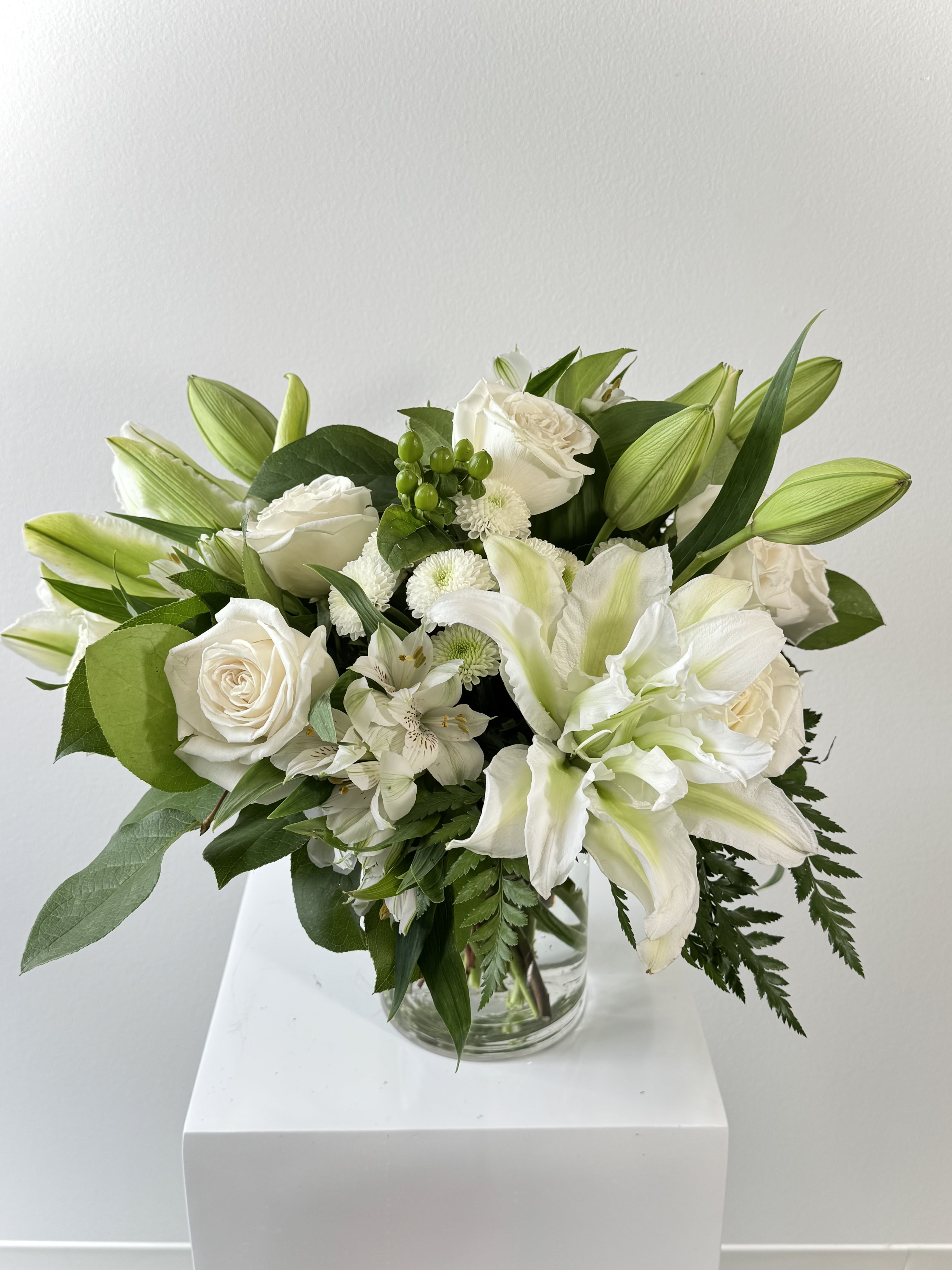 White Day - White Day Flower Arrangement – Pure White Lilies, Roses &amp; Cushion Mums Bouquet: Embrace serenity with the White Day arrangement, a pristine all-white masterpiece featuring white lilies, classic white roses, fluffy white cushion mums, delicate white alstroemerias, fresh green hypericum berries, and glossy lemon leaves. This elegant bouquet radiates peace, purity, and renewal—ideal for sympathy, weddings, baptisms, or minimalist luxury décor.  Why White Day Shines: Hand-crafted with fragrant white lilies for restored innocence, timeless white roses symbolizing new beginnings, textured white cushion mums for optimism, long-lasting white alstroemerias evoking devotion, and green hypericum berries plus lemon leaves adding natural contrast. Delivered in a sleek glass vase. Perfect for sympathy white flowers, wedding all-white bouquets, new baby gifts, or corporate elegance.  Bloom Symbolism: White Lilies: Purity, rebirth White Roses: Innocence, loyalty White Cushion Mums: Truth, hope White Alstroemerias: Friendship, prosperity Green Hypericum: Protection, energy Lemon Leaves: Freshness, zest  SEO-Optimized Keywords Search white day flowers, all white lily rose bouquet, white cushion mums alstroemeria, green hypericum sympathy arrangement, or lemon leaf white delivery? White Day tops pure white floral gifts, same-day sympathy bouquets, wedding white arrangements, and monochromatic luxury flowers.