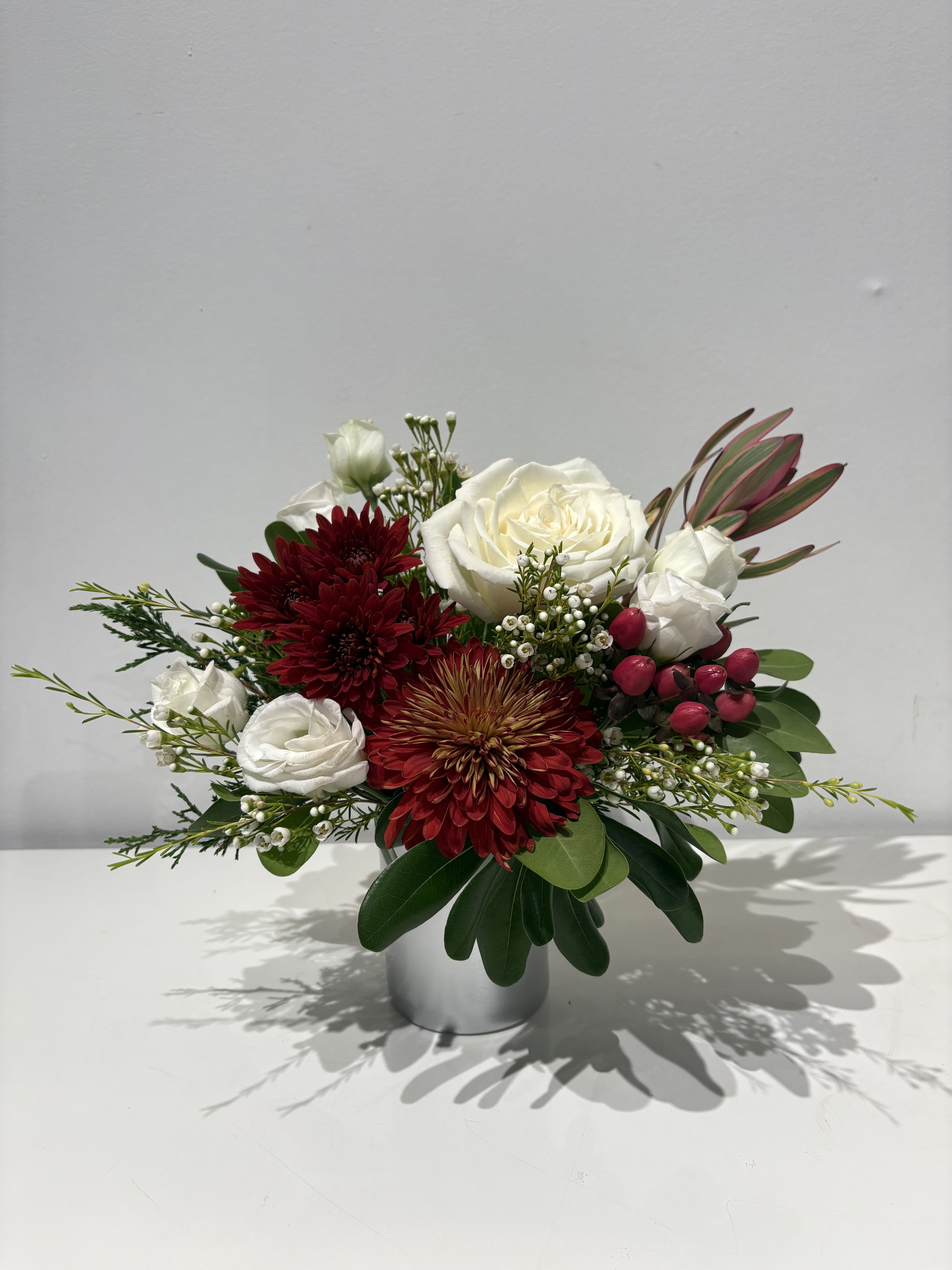 Host With The Most Gift - A glass cup holding an array of fresh cut Florals in seasonal colors. Mix of Mums, Roses, Alestro, and Button Pom adorned with sprigs of green and pine, make the perfect gift to say &quot;Thank for for hosting this holiday”. Also great for a small table of 4 or order a few to dot down a long table. 