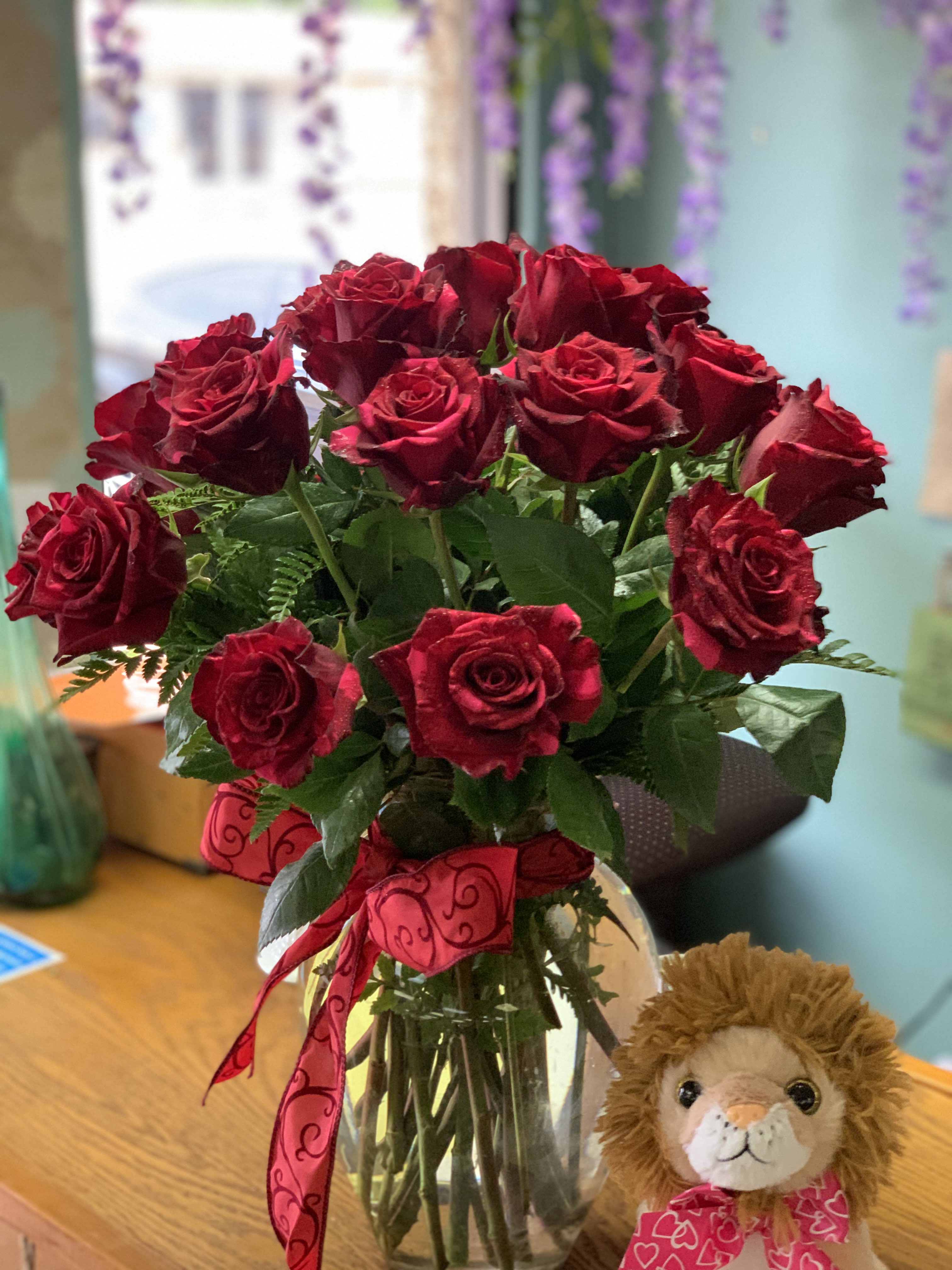 Eighteen Red Roses in a Vase - This beautifully arranged floral enchantment features 18 red roses with assorted greenery and is accented with rose petals inside the vase. 