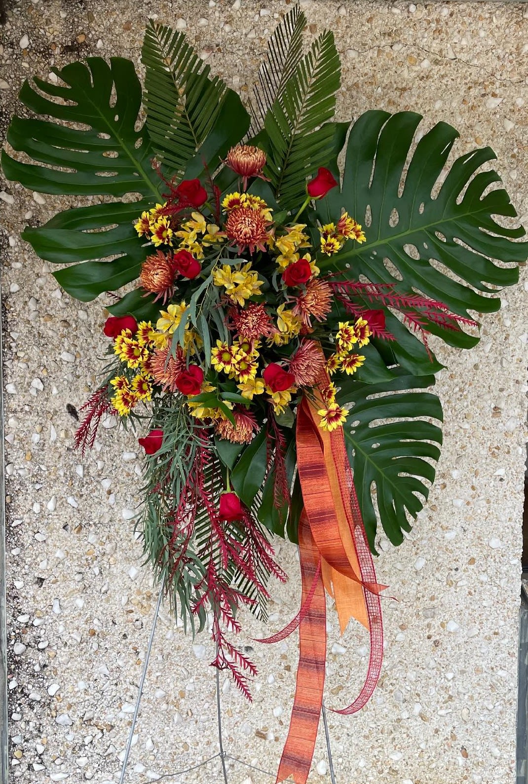 Big John - This awsome tribute spray features large Monastera Leaves, Roses, Mums and Fall Filler flowers. Sure to make a statement.