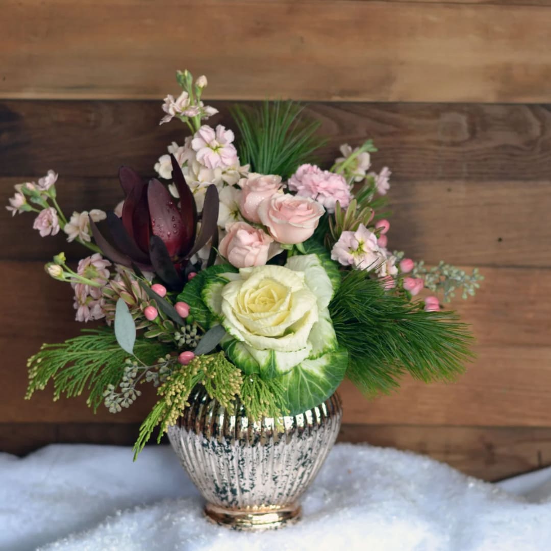 Snow Kissed  - Step away from the red and green this year. This breathtaking Snow Kissed bouquet is an elegant way to express your wintery emotions. Suitable for nearly any occasion, this design is available in two different size variations (standard and deluxe).  Mercury glass vase filled with pink spray roses, ornamental cabbage, pink stock, leucadendron, pink hypericum berries, and seasonal greens. 