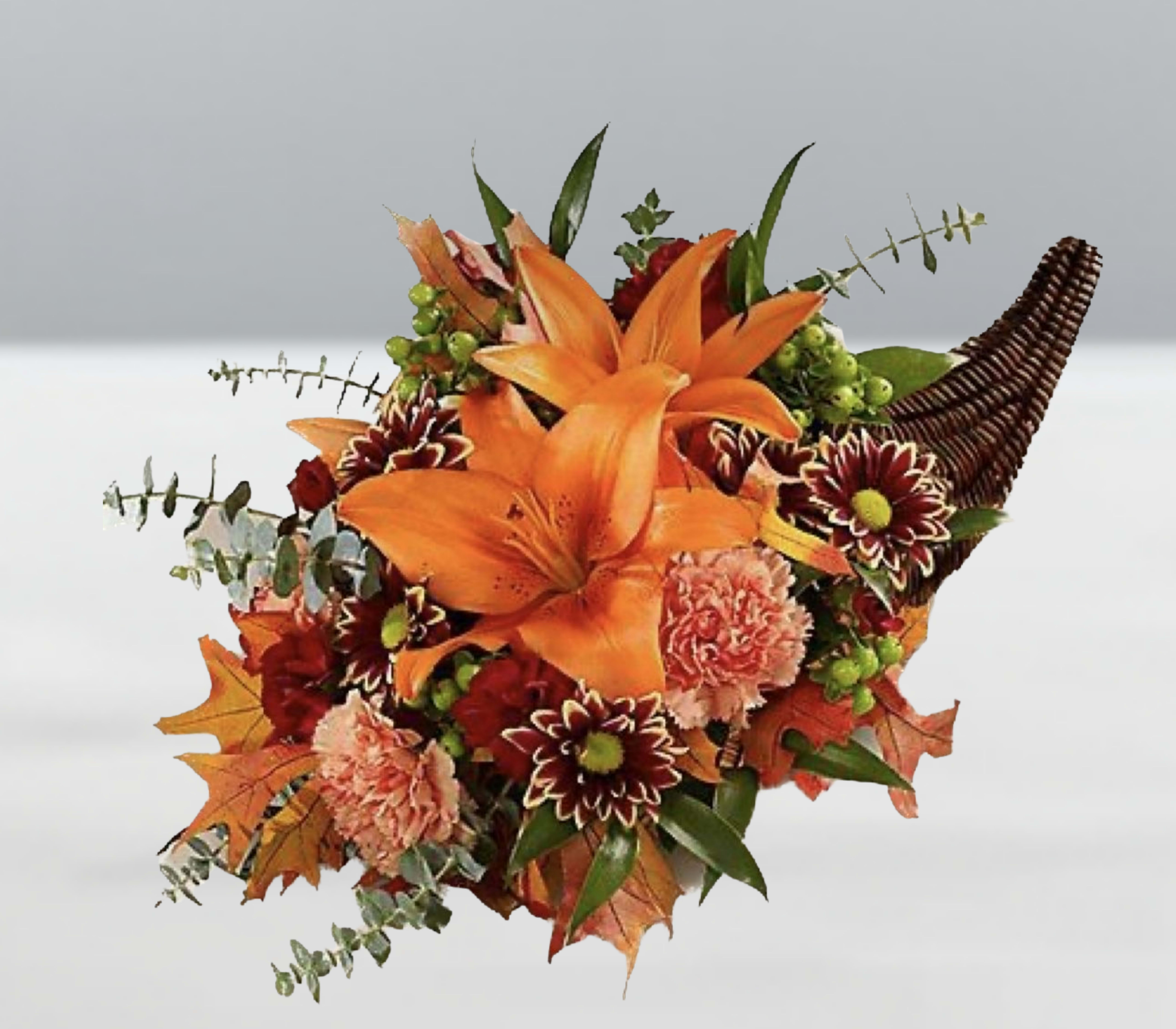 Cornucopia Glow -  Cornucopia Glow  A celebration of autumn’s golden hour—this woven horn overflows with orange lilies, peach carnations, crimson mums, and creamy blooms, accented by eucalyptus, maple leaves, and green berries. Each element catches the light like a flicker of gratitude, creating a soft, radiant glow that warms any space. Cornucopia Glow is a tribute to abundance, beauty, and the quiet magic of the harvest season.