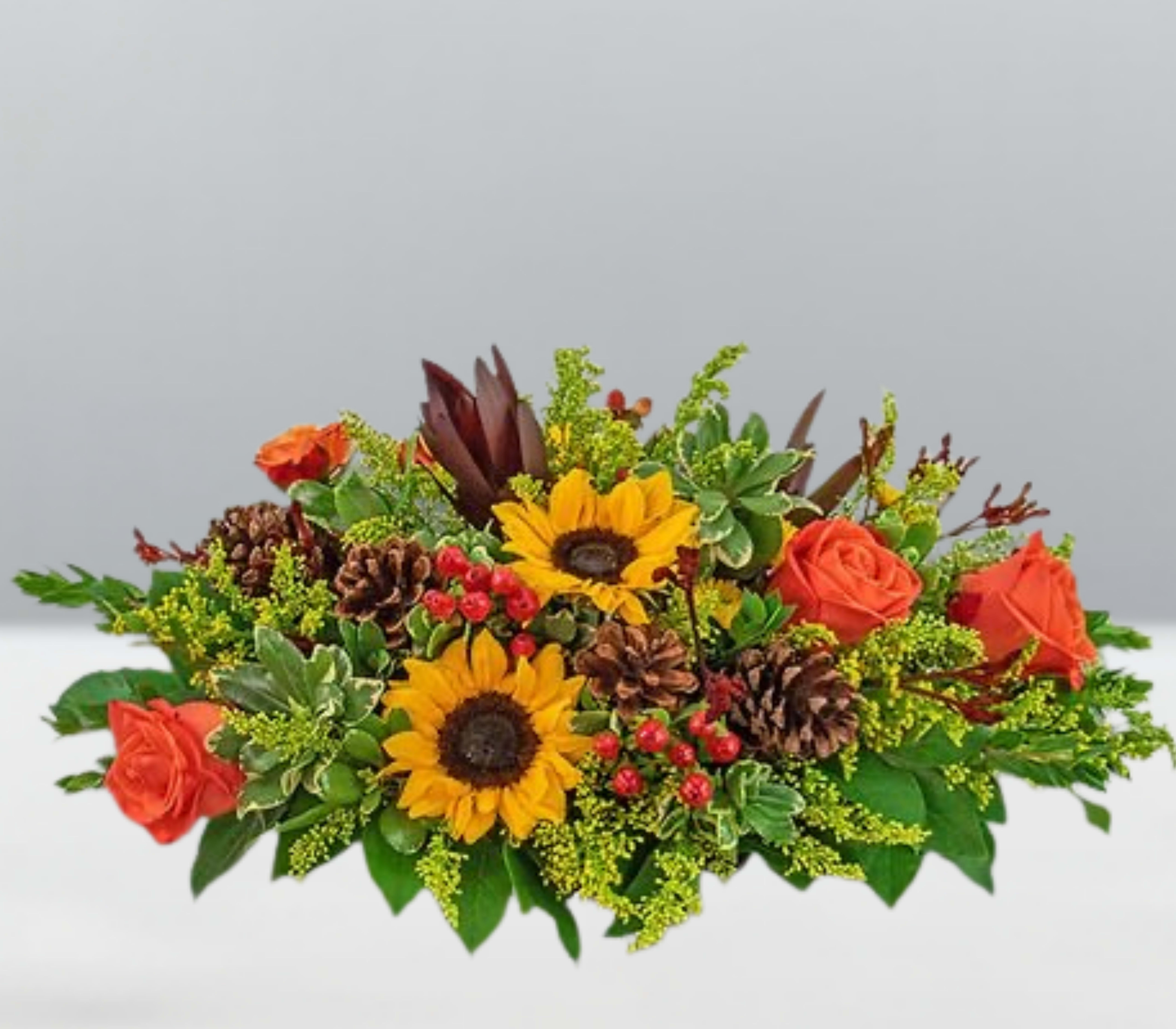 Grateful cove -  Grateful Cove  Nestled in a haven of harvest hues, Grateful Cove blends golden sunflowers, amber roses, pinecones, and berry accents into a lush display of seasonal serenity. With rich foliage and earthy textures, this arrangement evokes the feeling of a quiet woodland retreat—where gratitude grows wild and beauty gathers softly. Designed to warm hearts and tables alike, it’s a floral escape into the soul of fall.