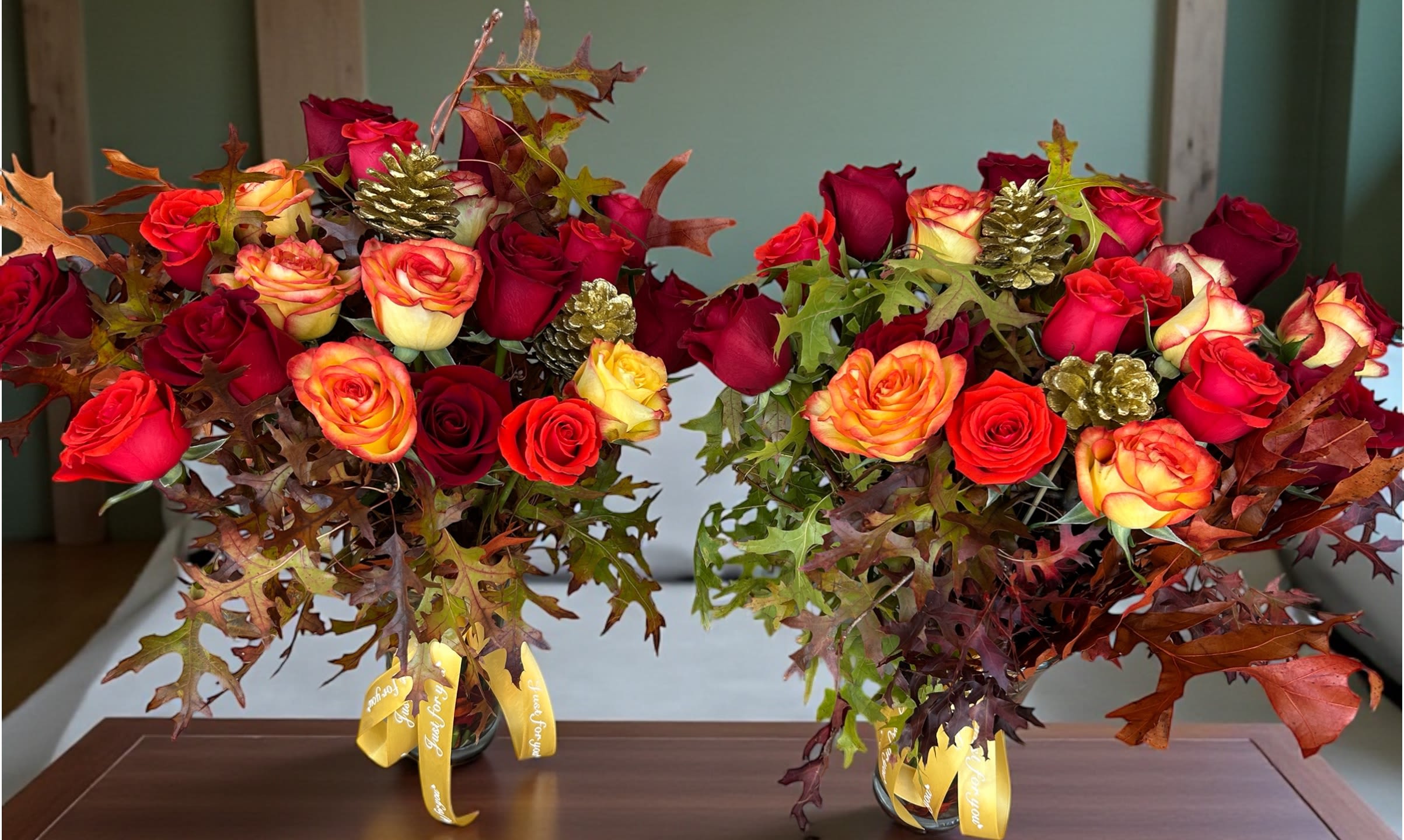 Autumn Harvest Rose Vase Duo - Celebrate the beauty of fall with this handcrafted rose arrangement duo. Featuring a rich blend of red, orange, and yellow roses accented with autumn oak leaves and golden pinecones, these twin vases bring a warm seasonal charm to any home or celebration. Perfect for Thanksgiving, dinner tables, office décor, or festive gifts.