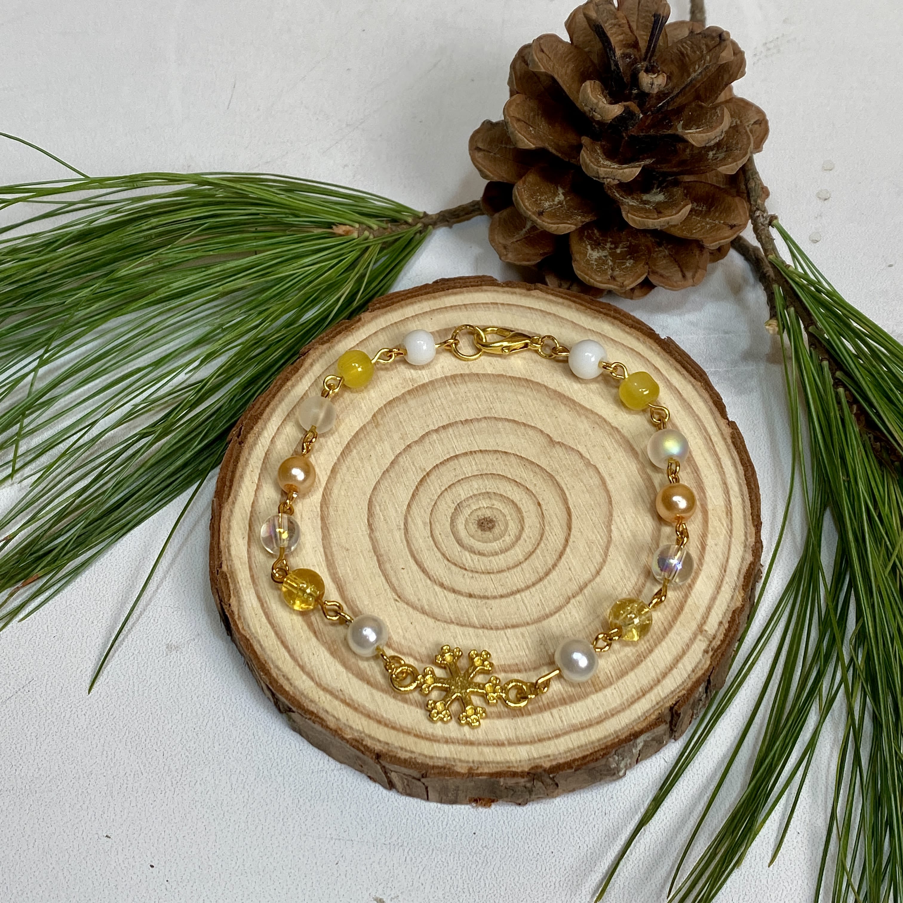 Golden Glimmer Snowflake Bracelet - Our Golden Glimmer Snowflake Bracelet is the perfect way to spread some brilliant cheer this winter! Featuring a gold plated snowflake charm, gold and white glass beads, and a clasp to keep your bracelet secure, this is a beautiful gift for someone you care about, or as a nice way to treat yourself! Bracelet handmade by Sunshine Orchard Designs.