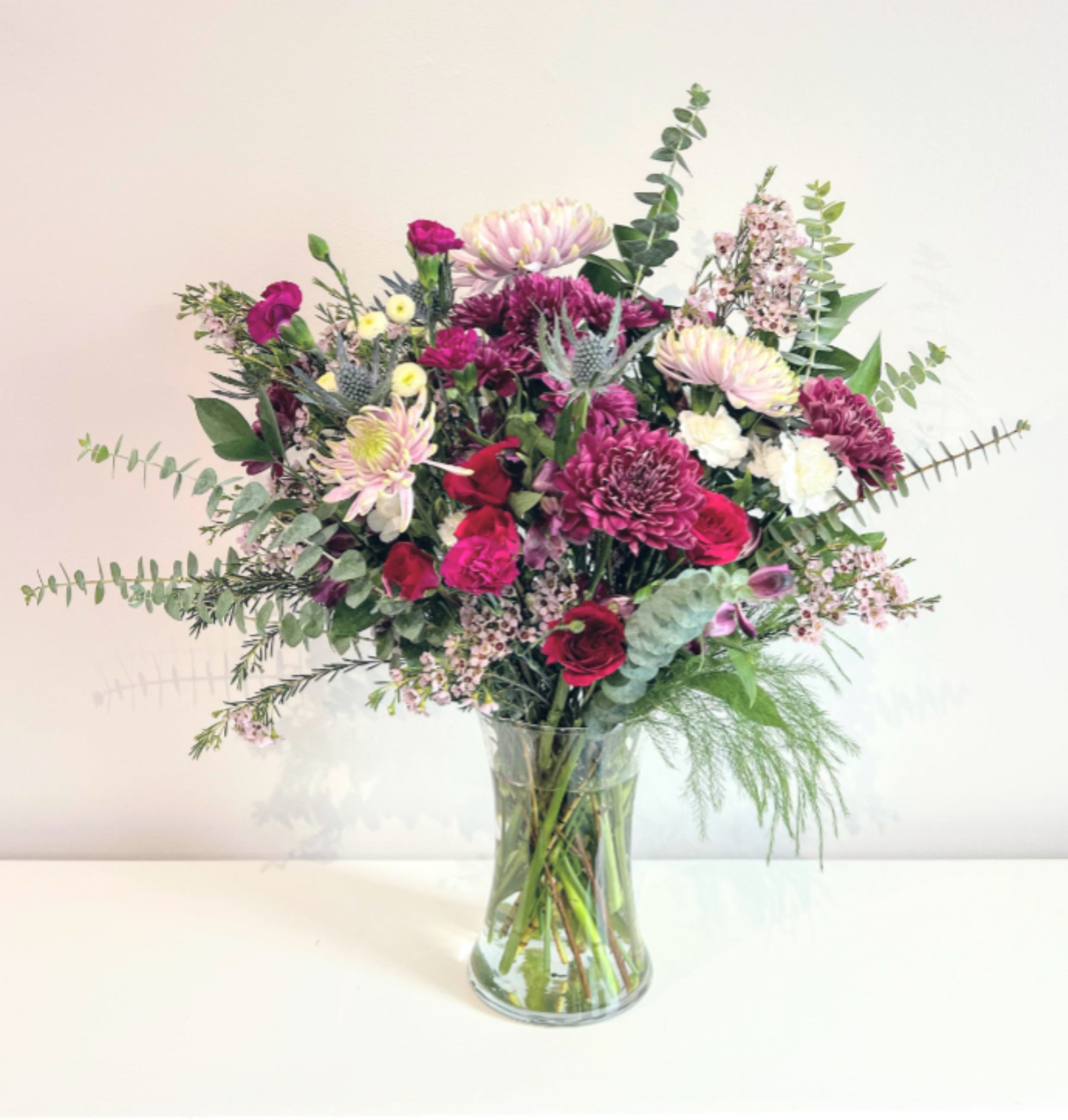 Something Wild - A wildly lush bouquet showcasing the best seasonal blooms in burgundy, purple, lavender &amp; white with a pops of red. Accented with lots of fragrant spiral eucalyptus &amp; dark greens. Arranged tall &amp; natural in a clear glass gathering vase. It's the perfect floral gift for any special occasion.  Measures approx. 19&quot; tall and 16&quot; wide Orientation: All around