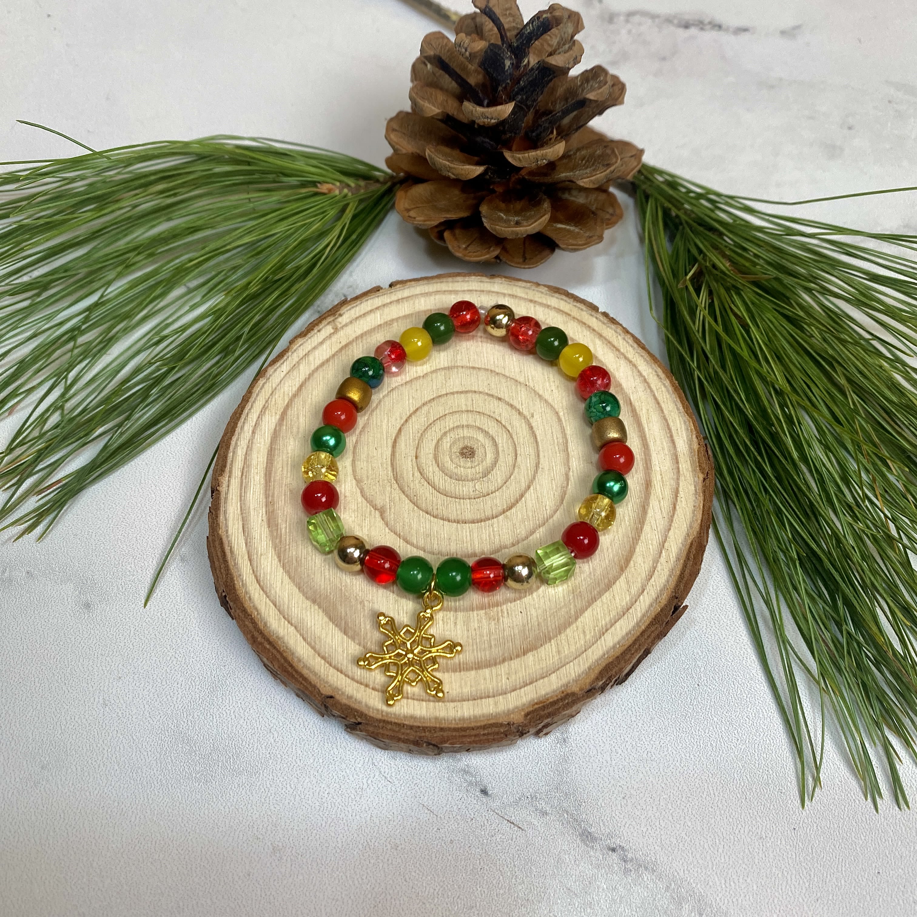 Classic Cheer Gold Snowflake Bracelet  - The Classic Cheer Gold Snowflake Bracelet is a great gift for this holiday season! Featuring a gold plated snowflake charm, and red, green, and gold glass beads on an elastic string, this bracelet just screams Christmas! Bracelet handmade by Sunshine Orchard Designs