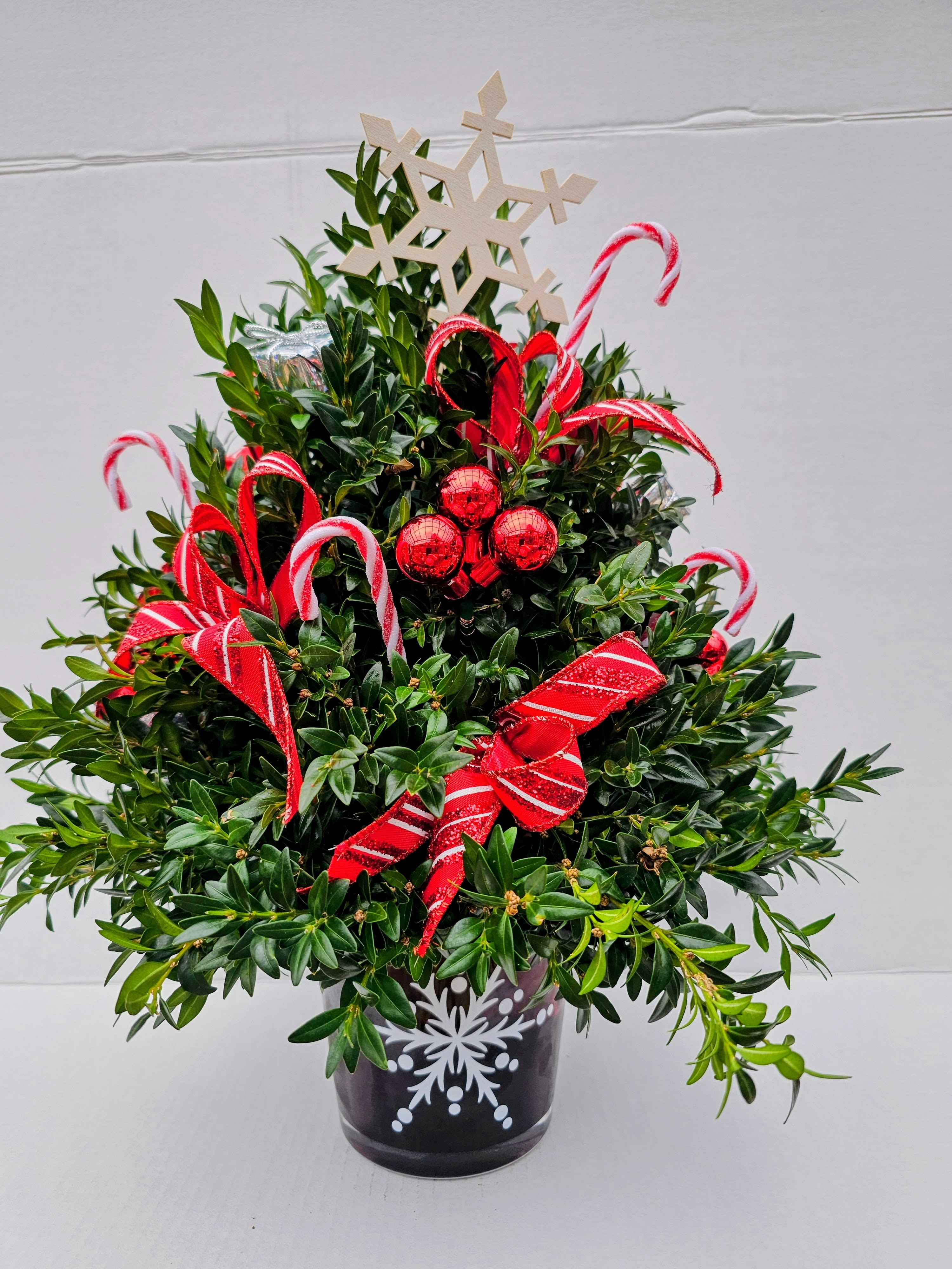 Winter Wonderland Boxwood tree  - Cut Boxwood branches arranged as a tree shape in a glass vase w/ snowflake . Adorned with tiny ornaments,bows and flowers. 