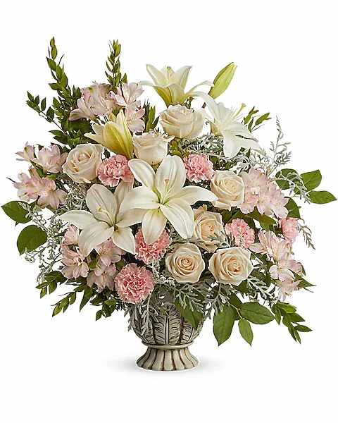 Teleflora's Peaceful Joy Bouquet - A peaceful yet powerful showing of support and love, this dramatic rose bouquet is presented in a classic urn. This bouquet features crÃ¨me roses, white asiatic lilies, light pink alstroemeria, pink carnations, silver lace dusty miller, lemon leaf and myrtle. Delivered in a Thoughtful Tribute Pot.