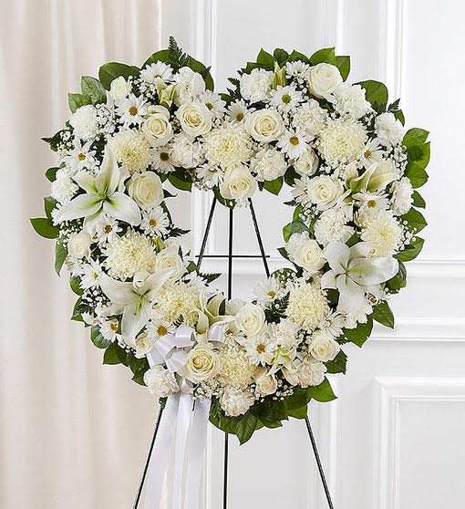 Standing Spray All White Heart - Our standing, open heart-shaped arrangement in all white, Handcrafted with an assortment of flawless white blooms, it is a magnificent tribute fitting for the funeral services. Open, heart-shaped arrangement of all white roses, hybrid lilies, football mums, carnations and daisy poms; accented with baby’s breath and soft, lush greenery. Arrangement is designed on an easel and accented with satin ribbon.