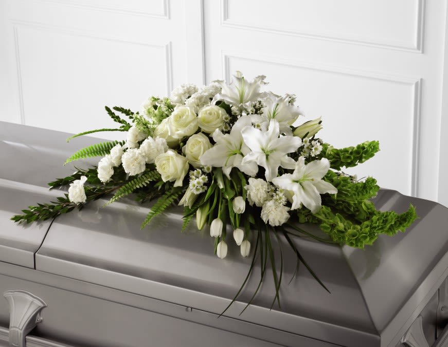 White Casket Spray -  White Casket Spray inspires thoughts of comfort and peace to those wishing to pay their respects for the loss of the deceased. White roses, snapdragons, Oriental lilies, larkspur, carnations and are accented by the bright green stems of Bells of Ireland and an assortment of the finest lush greens to create the perfect arrangement to display on the top of their casket during their final farewell service. 
