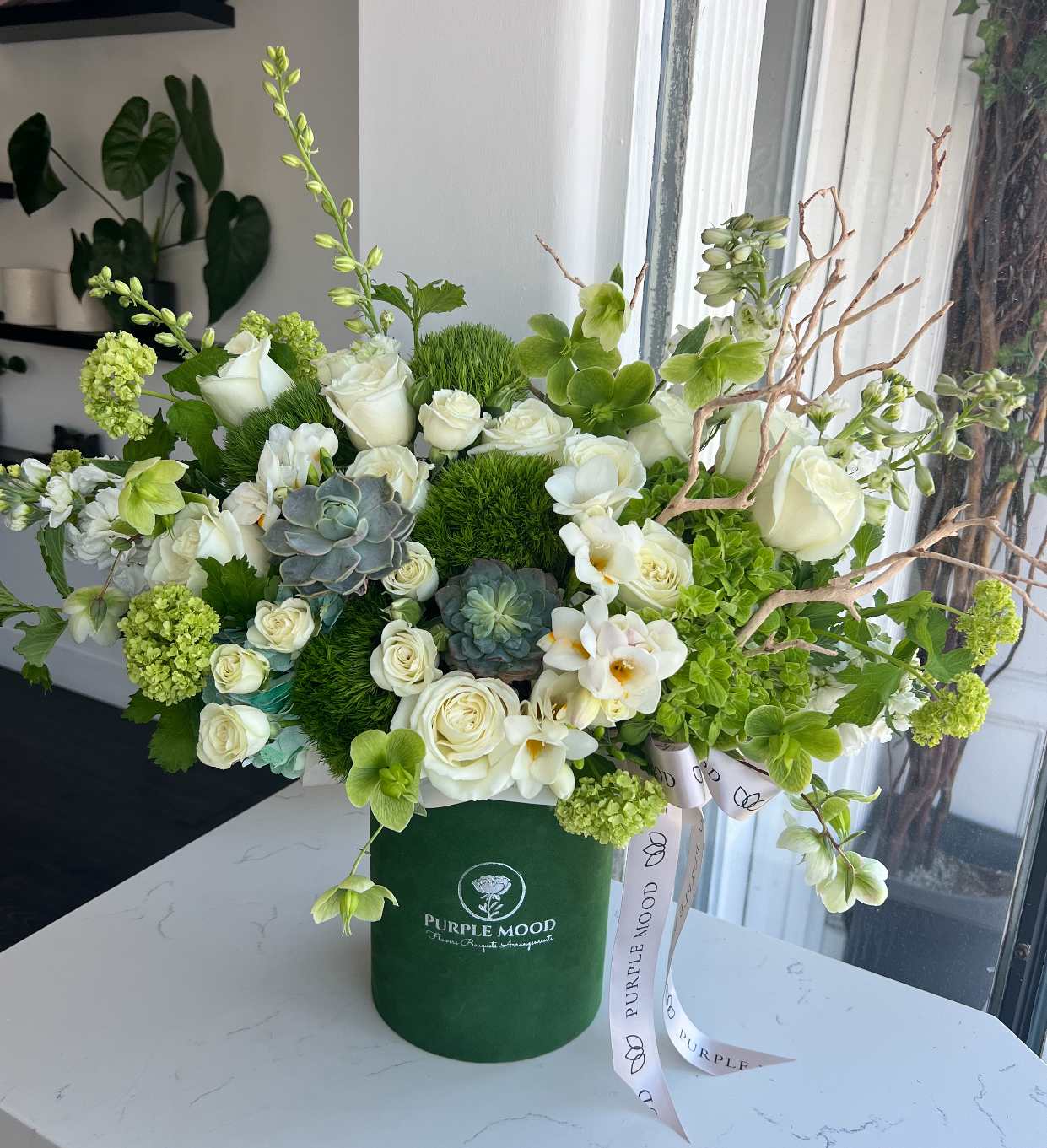 Nature Green Box - Container size - D6.75'x H7.5'  Bring the outdoors in with the Nature Green Box, a lush blend of soft whites, vibrant greens, and textured accents. Designed in a deep green velvet hat box, this arrangement has a fresh, earthy feel — perfect for nature lovers or as a modern décor statement.  Key Features:     •    Presented in a deep green velvet hat box     •    Finished with an elegant ribbon for a refined look     •    A refreshing mix of textures and natural tones     •    Great for home styling, birthdays, or thoughtful gifts