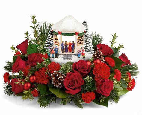 Thomas Kinkade Sweet Sounds of Christmas Bouquet - Thomas Kinkade’s Sweet Sounds of Christmas collectible features a group of cheerful carolers standing beneath a softly lit gazebo. The carolers and the gazebo are decked in their holiday best and white snow glistens on the ground and trees. The keepsake collectible sits atop a centerpiece of fresh evergreens. Red flowers, pine cones, and ornaments peek out from the greens. Add the Sweet Sounds of Christmas to your collections or start a new tradition with someone you care about this Christmas.  