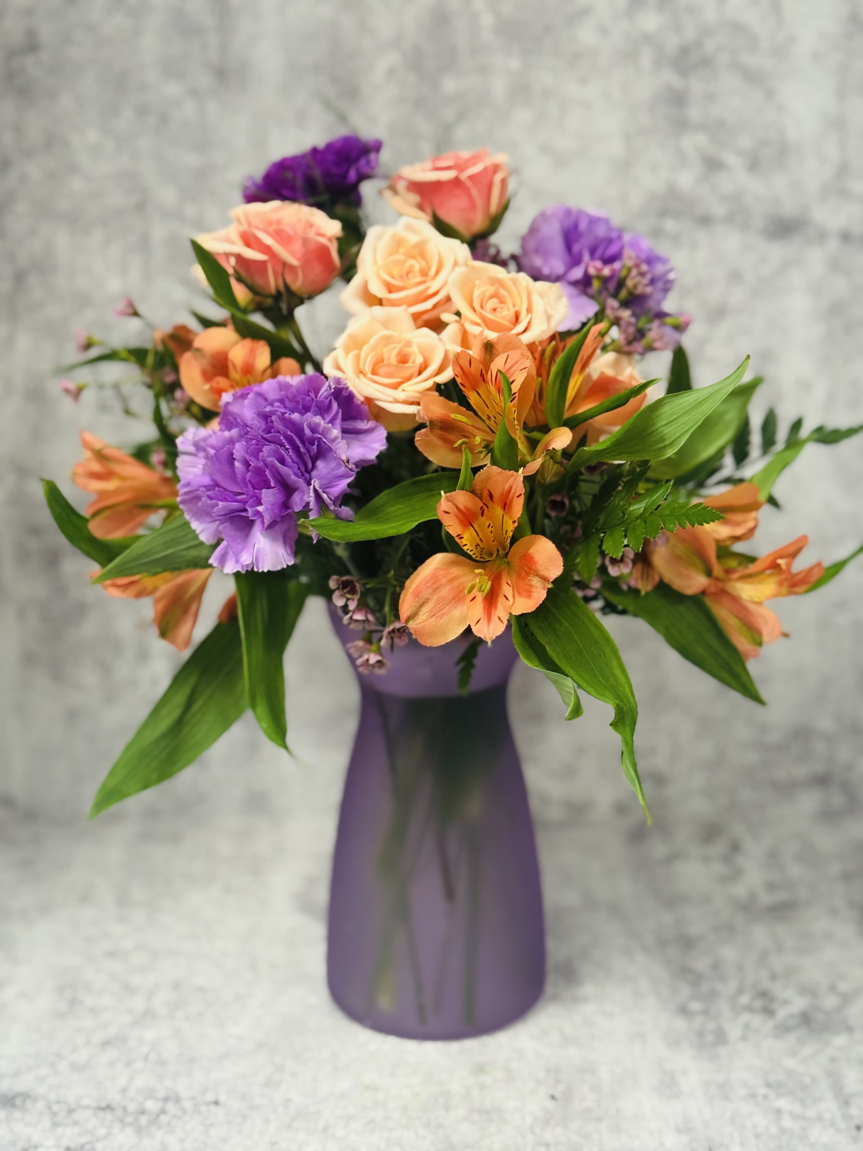 Pastel Delight - Colored Vase with coordinating flowers to match! Spray Roses, Carnations, Alstromeria, filler &amp; greenery.  We will coordinated the vase with the flowers available!  A practical, long-lasting arrangement!