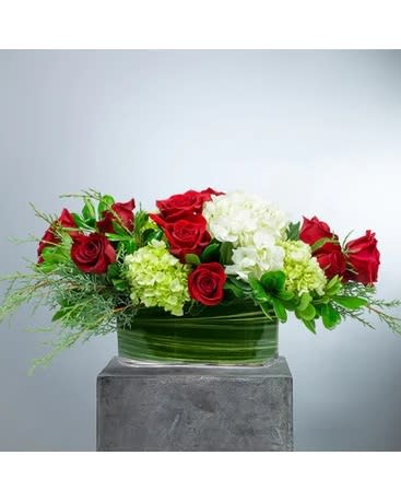 Always Centered on Christmas - Modern and enchanting. Always Centered on Christmas will take center stage on your table or island. This centerpiece style arrangement designed in a low, long clear glass container with traditional red, green and white color scheme in blooms like hydrangea and roses with seasonal greenery. Approximately 30&quot; W X 9.5&quot; H   All prices in USD ($)  Standard  DGTMF-1243