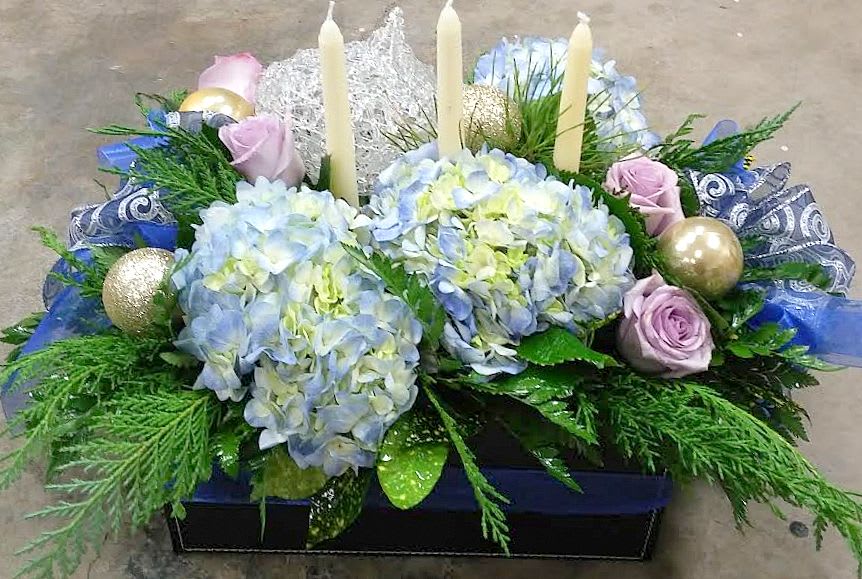 Blue and purple holiday. - This gorgeous arrangement with blue hydrangea and purple roses, adorned with ribbons, holiday greens, and candles, is a wonderful gift for the holidays. Give them something grand!