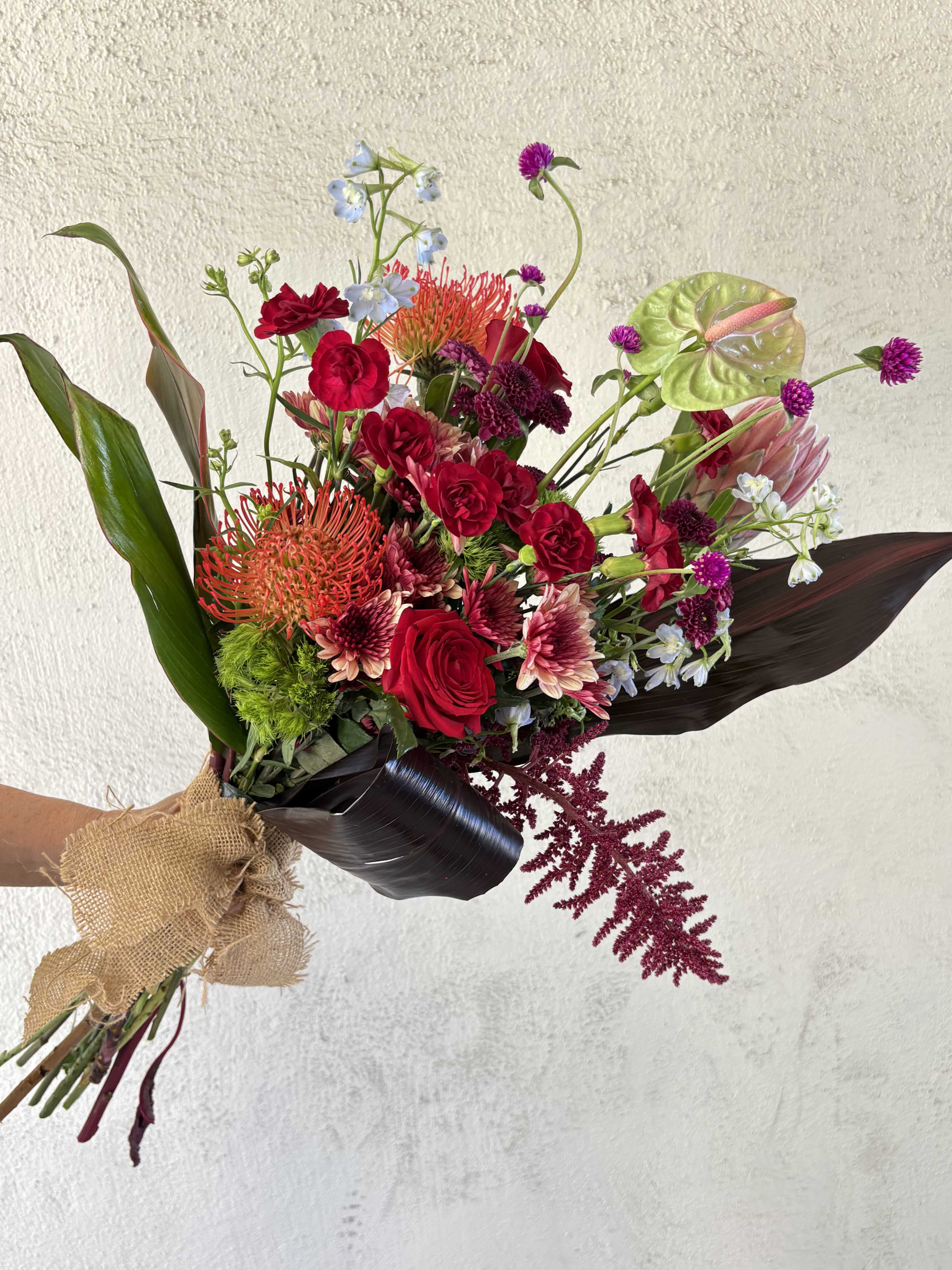 FRESH WEEKLY DROP 1 - This drop includes Anthurium, Protea pincushion and tropical, Amaranthus, Dianthus, Red Roses, Buttons, Chrystanthemums, Delphinium, Globe Amaranths, Red Carnations, and leaves.  Purchase standard for hand-held bouquet wrap and deluxe for bouquet designed in a vase.