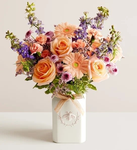 Honey Bee Buzz - EXCLUSIVE Get them buzzing with our charming bouquet! A garden-fresh gathering of blooms in sweet shades of lavender, purple, peach and pink come together for a mix of color and texture. Designed in our Sweet As Can Bee artisanal vase, featuring an adorable honey bee and raffia bow, it’s a gift that adds quaint beauty to any decor.