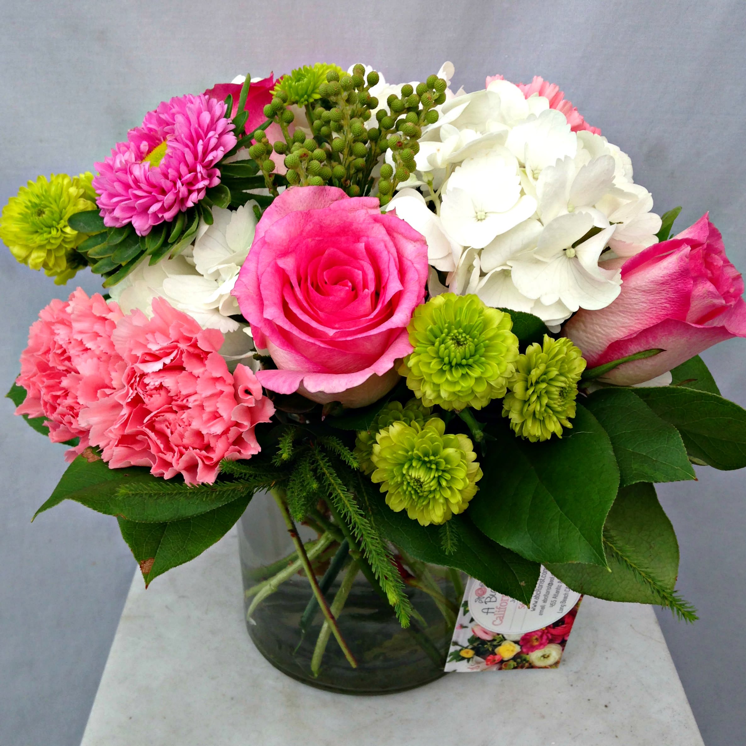 Pink and Green - Beautiful pink roses, green button and white hydrangea, lush greens in compact cylinder vase. An excellent color combo for that special someone. Fits well on desk or end table. Standard - pictured Deluxe - We'll add more beautiful blooms  Premium -  Even more premium blooms in larger vase!