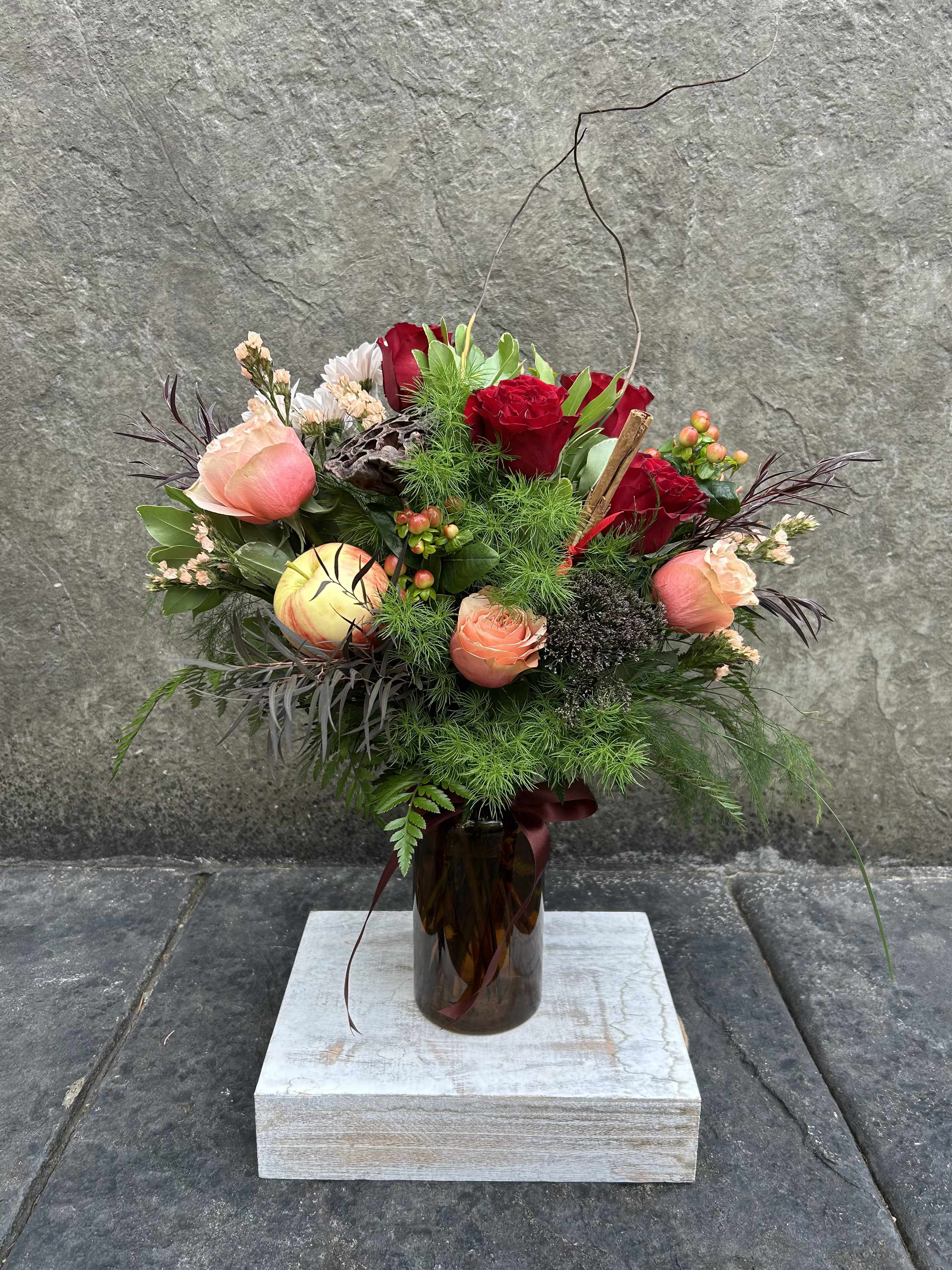 Apple Cider - Welcome the cold crispy air with our warm apple cider! Red hearts roses, peach roses, berries, chrysanthemums, lotus pod, curly willow, blooming filler, and a mix of greenery in a brown glass vase  with cinnamon  stix and a apple.   *Reasonable substitutions may be made due to floral availability, will have same overall look and feel.