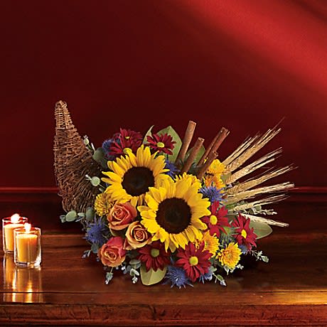 Classic Cornucopia -  sunflowers and orange roses are accented with unique blue eryngium, red daisies, yellow cushion mums, eucalyptus and magnolia leaves in a wicker cornucopia-shaped basket.