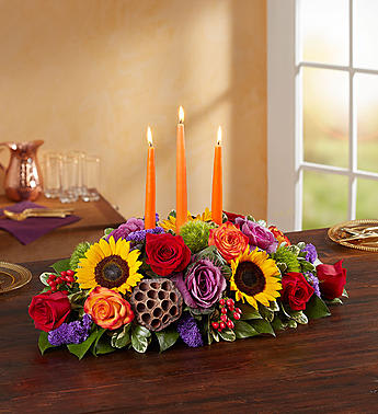 Garden of Grandeur for fall centerpiece   - All-around centerpiece arrangement with red and circus or bi-color orange roses; sunflowers; red hypericum; purple statice and kale; accented with assorted greenery and dried lotus pods