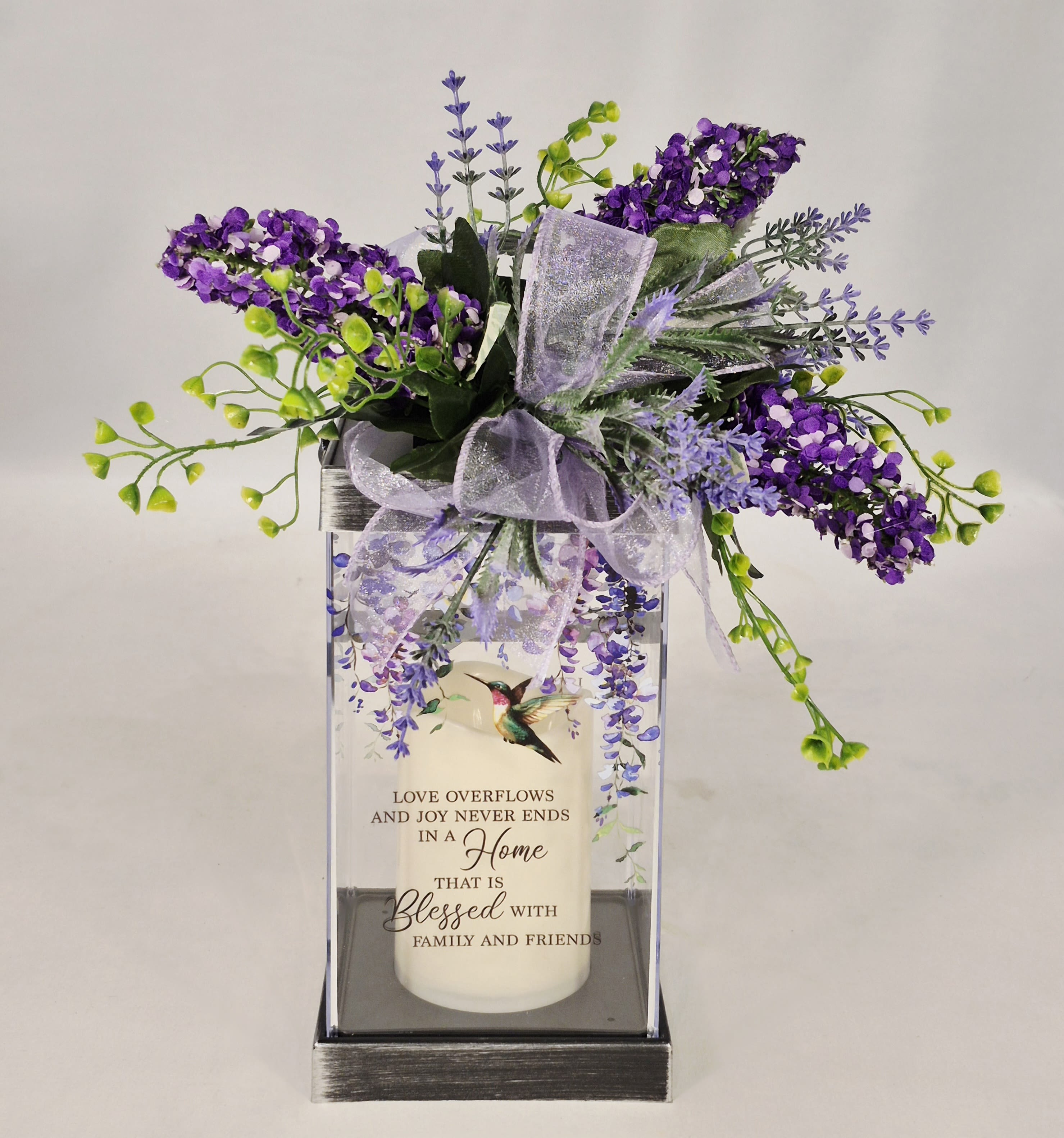 Blessed Lighted Lantern with Silk - Blessed lantern is a beautiful flameless LED Candle Lantern made with high-quality polyresin finish with a built in automatic timer. Comes adorned with a lavender bow and beautiful silk arrangement. Wonderful gift for housewarming, birthday or just because.   6 hours ON/18 Off (3 AAA batteries included)  W: 4.75&quot; H: 13&quot; D: 7.75&quot;
