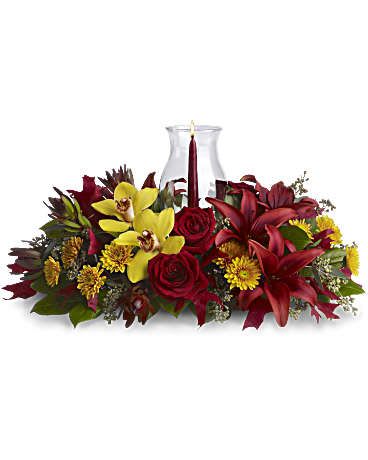 Glow of Gratitude Centerpiece - Give thanks by sending this fall flower centerpiece. A chic, exotic spin on the traditional Thanksgiving centerpiece, it features orchids, roses, lilies and leucadendron in rich fall colors below a glowing taper candle, surrounded by a glass hurricane. Yellow cymbidium orchids, red roses, burgundy asiatic lilies, bronze cushion mums, red leucadendron, seeded eucalyptus and salal are accented with red oak leaves. A pomegranate taper candle inside a classic glass hurricane adds a warm glow to the room. Orientation: All-Around