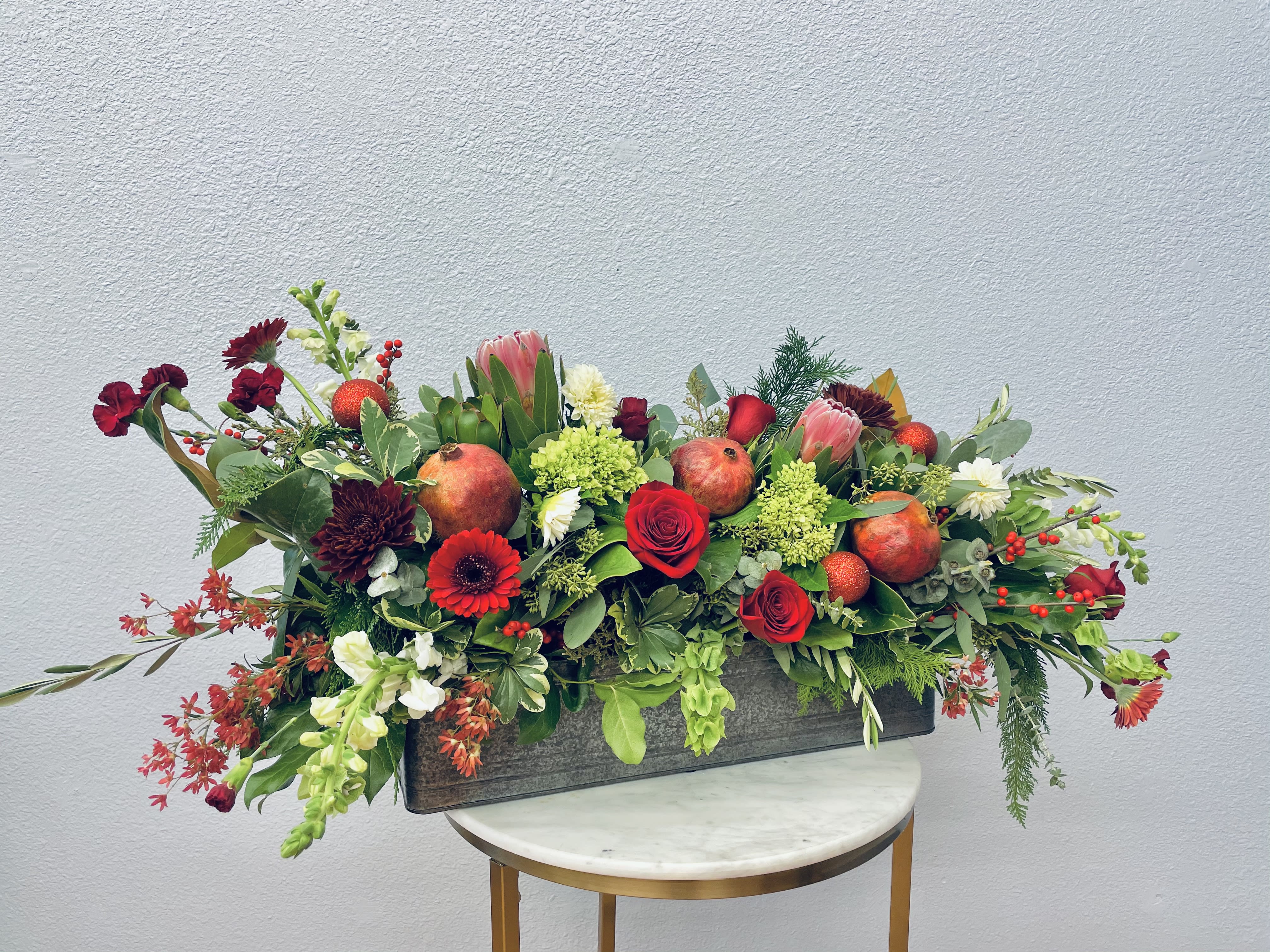 Tannenbaum - Striking and fun!  This holiday box boasts gorgeous protea, pomegranate, sparkly ornaments and festive berries with roses and seasonal flowers in deep hues. Set in a wooden planter box with botanical eucalyptus, magnolia and cedar, this is a best selling stunner! *Photo shows deluxe upgrade*