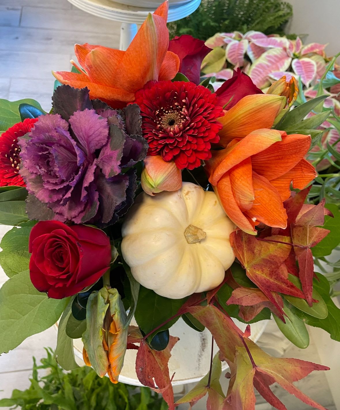 Brightly Fall - Roses, Gerbera poms, amaryllis, flowering kale, seasonal leaves and an ornamental pumpkin   in a round cylinder. 