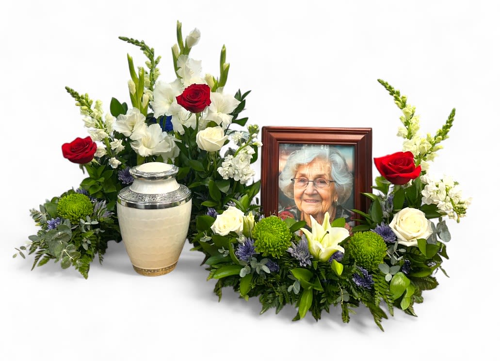 Serenity Surround Urn and Photo Memorial Arrangement - The Serenity Surround arrangement is a deeply heartfelt tribute, thoughtfully crafted to honor the memory of your loved one. It gently encircles their photograph and urn with soft, beautiful blooms such as white lilies and roses, symbolizing purity and love. Lush greenery weaves through the display, creating a peaceful and comforting presence. This arrangement is designed to offer a serene space for reflection, helping you find solace and remembrance during this difficult time. Urn and Photo not included. 