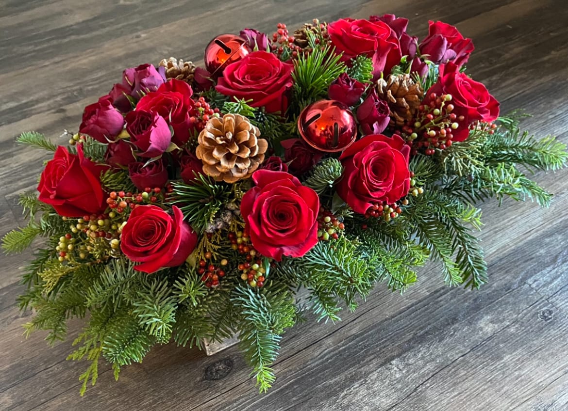 Christmas centerpiece - Red roses and Christmas berries, greens, pinecones and jingle bells in a rectangle wooden box. Greeting card with a handwritten message is included. Send the most beautiful flowers for that special someone. Same day delivery available to Tequesta, Jupiter, Palm Beach Gardens and Palm Beach.