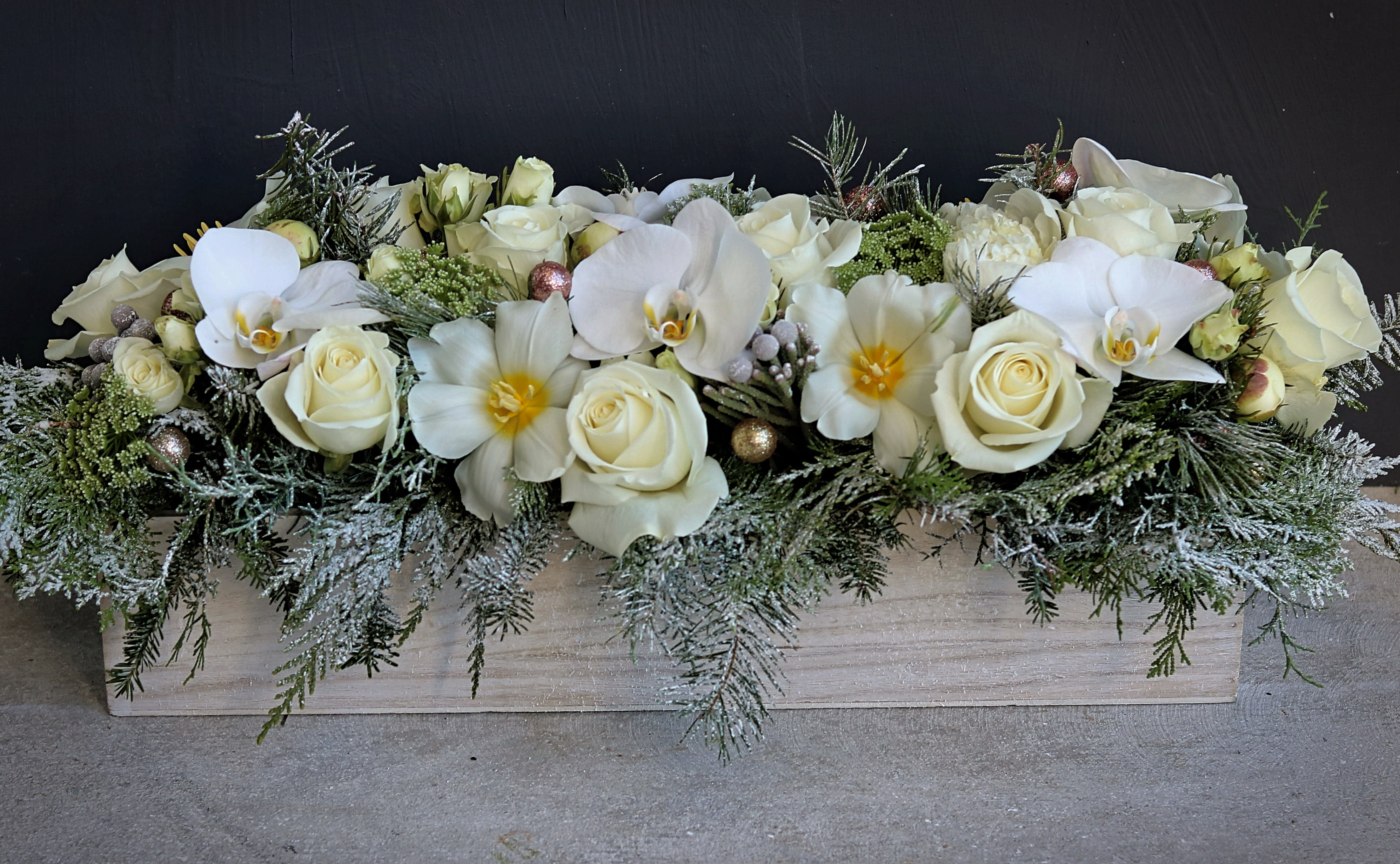 christmas centerpiece in wood planter - This Christmas centerpiece contains premium blooms such as peonies, roses, tulips, orchids and others surrender with Christmas greens covered in faux-snow. It's in a 20&quot; rectangle wooden planter. Next day delivery available to Tequesta, Jupiter, Palm Beach Gardens and Palm Beach.