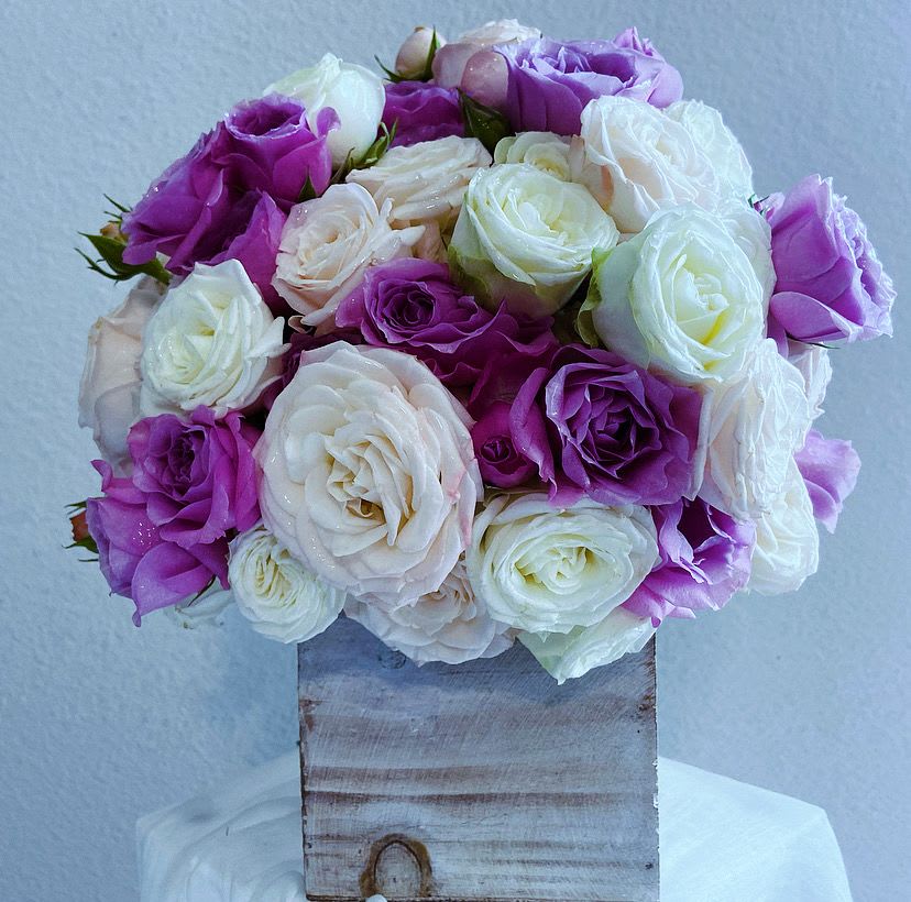 Call Me Rose, Triple Love - Discover the epitome of elegance and romance with our enchanting “Call Me Rose, Triple Love” arrangement, thoughtfully crafted to captivate the heart. This is an April May Flowers signature design that is a sequel, if you will, to the first two “Call Me Rose” designs in this series.   This exquisite display features an array of Bombastic miniature roses in soft pink, pure white, and lavender, each bloom radiating charm and grace.   Nestled in a rustic wooden box, these delicate roses create a stunning visual contrast that enhances the arrangement's romantic appeal. The varying hues blend beautifully, evoking feelings of love and serenity, making it a perfect gift for anniversaries, Valentine’s Day, weddings, or simply to express your affection.  Ideal for any setting, this arrangement transforms your space into a haven of beauty and warmth. Whether placed as a centerpiece or gifted to a loved one, it embodies the essence of romance and the delicate artistry of nature, inviting admiration and delight. Treat yourself or someone special to this timeless floral masterpiece.
