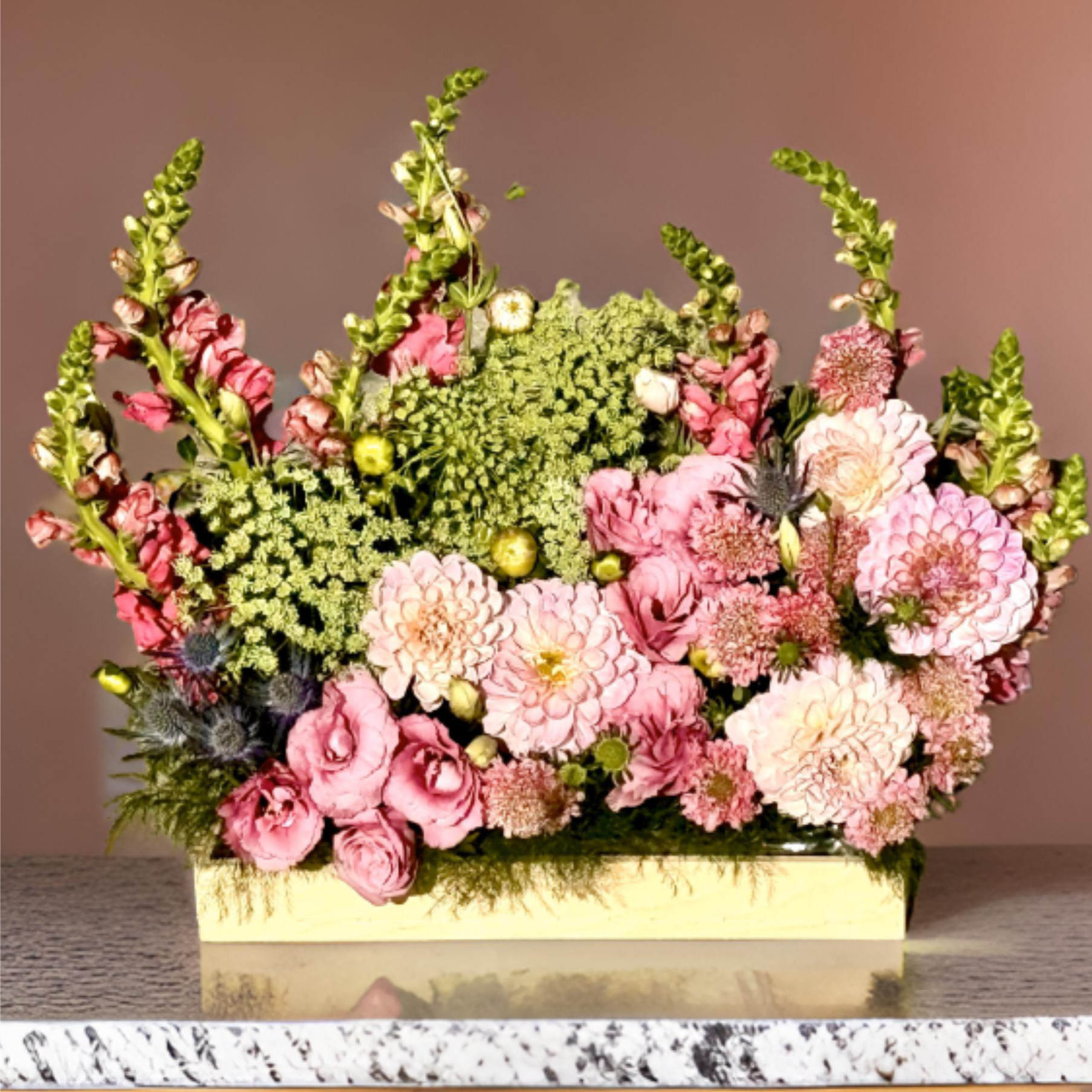 Pink Dahlia Arrangement - Bring a touch of elegance and romance to any space with this lush pink flower arrangement by Hollywood Blooms. Featuring stunning fully bloomed pink dahlias, delicate lisianthus, and airy seasonal greenery, this design is set in a natural wooden box for a fresh, garden-inspired look.  Perfect for birthdays, romantic gestures, housewarmings, or event centerpieces, this bouquet captures both softness and structure — blending ruffled petals, vertical movement, and rich textures.  Handcrafted by our expert florists in Hollywood, Los Angeles, this premium arrangement is available for same-day flower delivery across Los Angeles, including West Hollywood, Studio City, and Beverly Hills.  Whether you're sending a message of love, celebrating someone special, or decorating an event, this design brings joy and timeless floral beauty. Let us help you deliver unforgettable moments — one bloom at a time